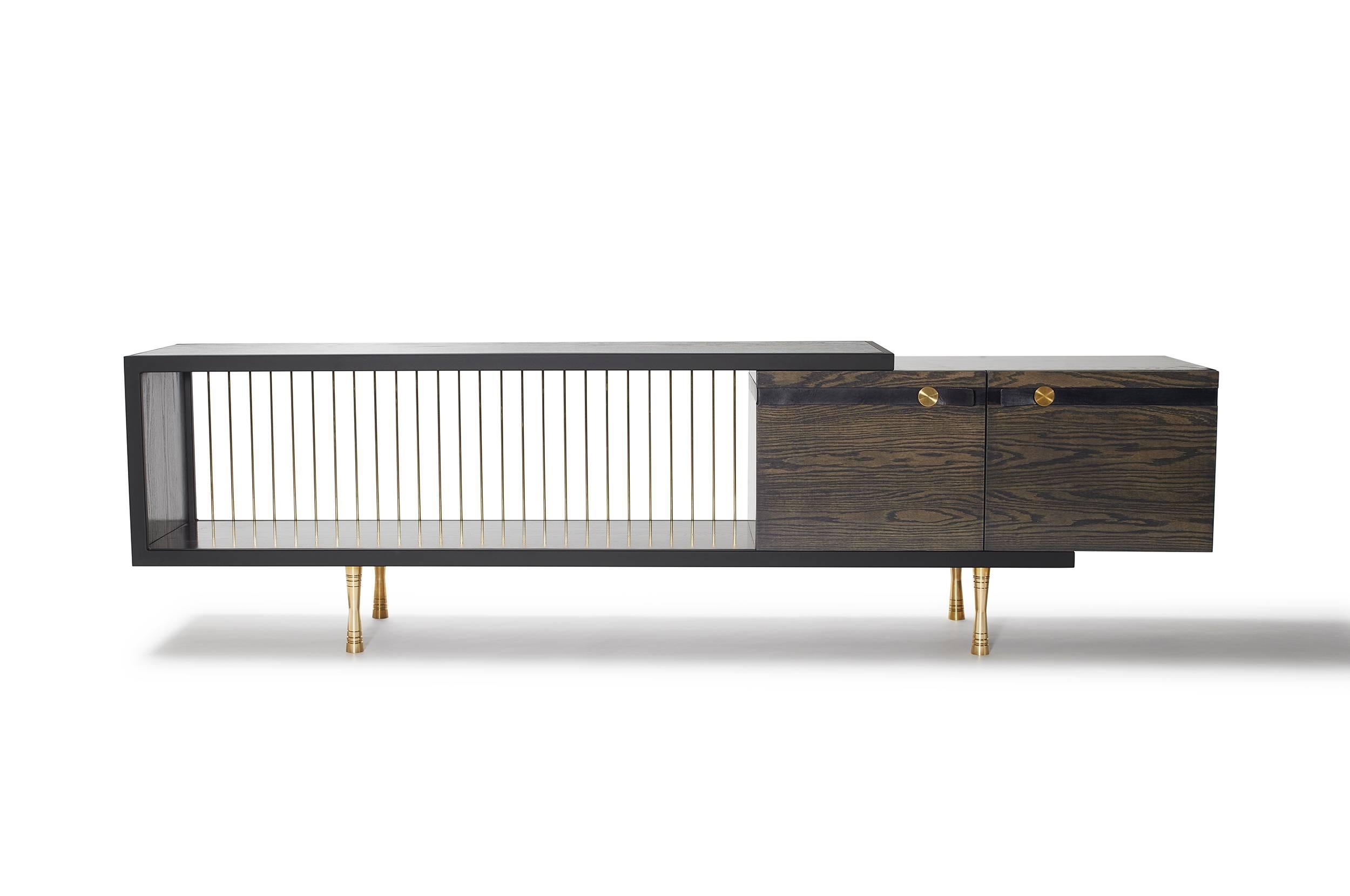 The Viga console features a handcrafted matte black powder-coated steel frame along with hand-dyed leather accents, dark grey stained red oak cabinetry and delicate brass rods lining the exposed back edge. Use as a credenza, bookshelf, media cabinet