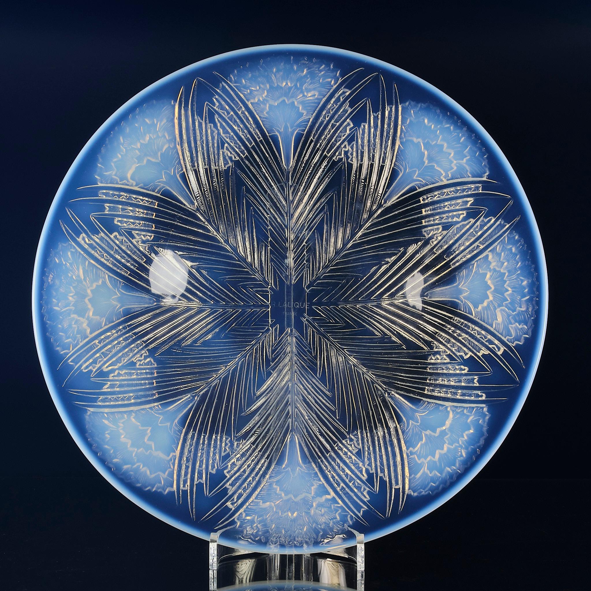 Splendido salverino in vetro opalescente Art Decor decorato con otto garofani fioriti a ventaglio affiancati da fronde disposte in cerchio, con una forte opalescenza blu cielo. Firmato R.Lalique.


