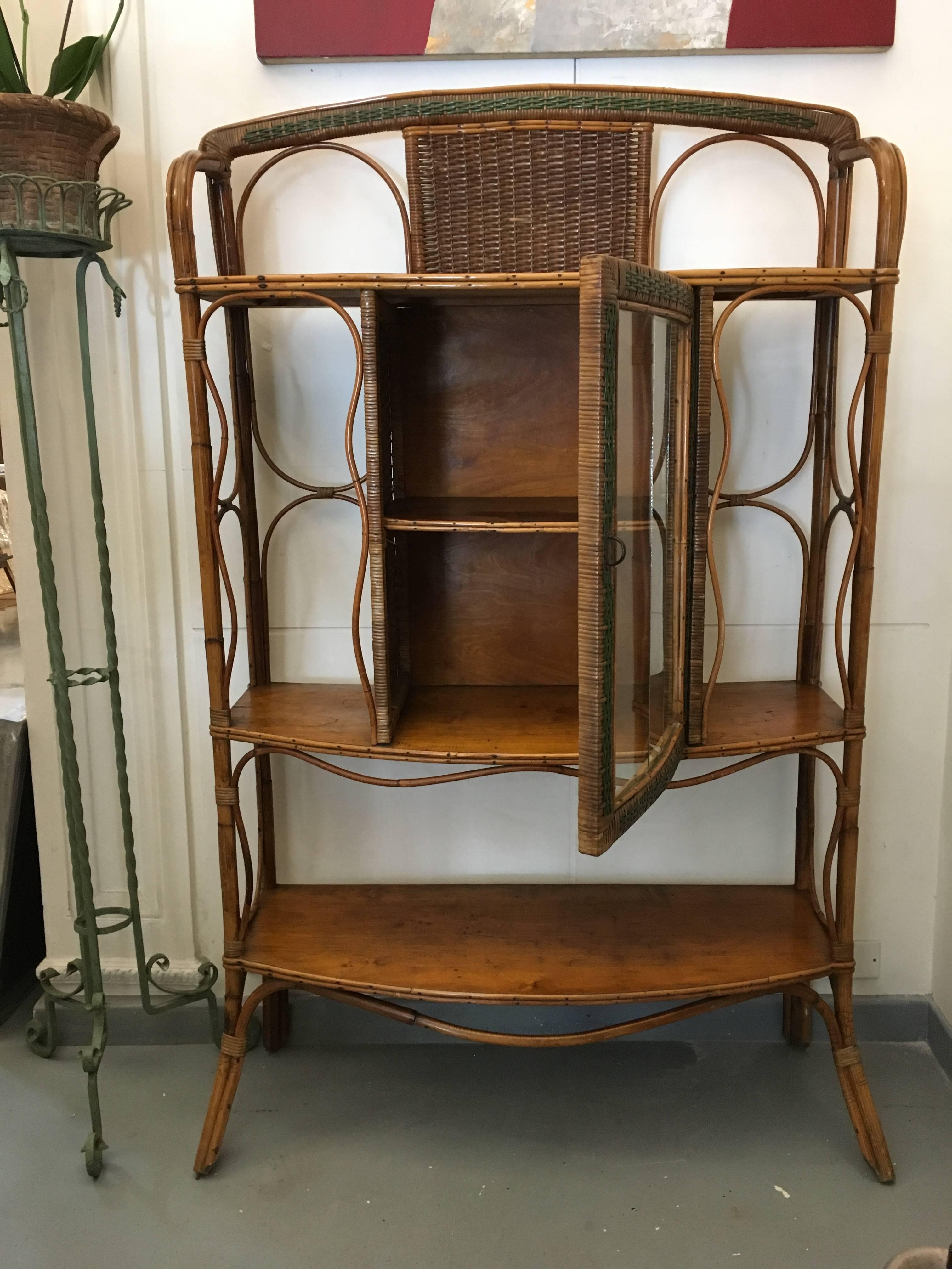 This wicker cabinet with three shelves and a central compartment with an interior shelf is decorated with green art nouveau details and is in the Colonial style.