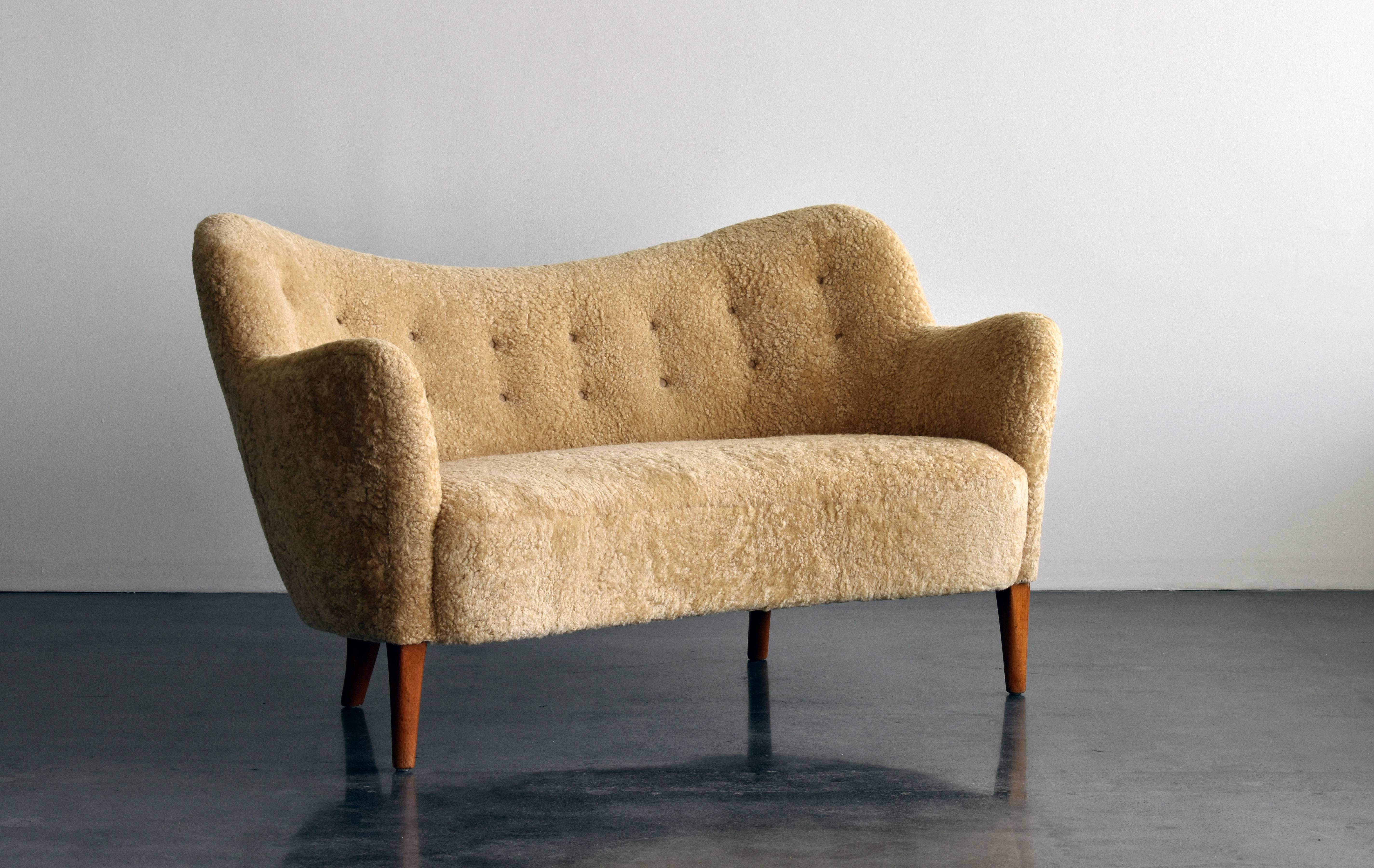 A sofa designed by Finn Juhl, executed by Carl Brorup in the late 1940s. Upholstered in beige sheepskin. 

The present model sofa is recorded in the digital furniture archives of the Danish Museum of Art & Design. Importantly note the tapered front