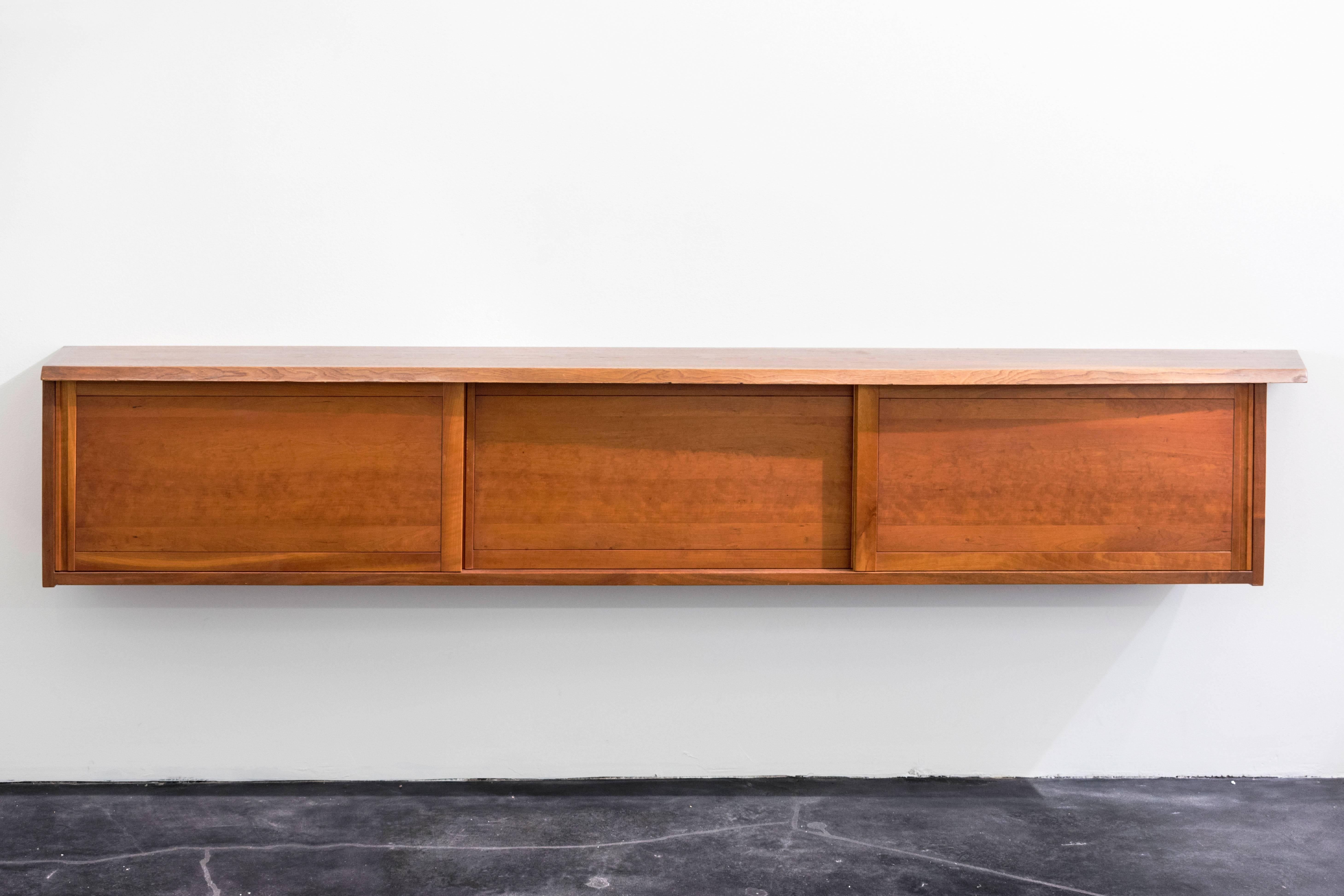 An American three-drawer walnut cabinet by George Nakashima. Handcrafted in Nakashima studios. Features sliding doors, interiors with three adjustable shelves. 

The cabinet presents the viewer with a front free edge, single side free edge and one