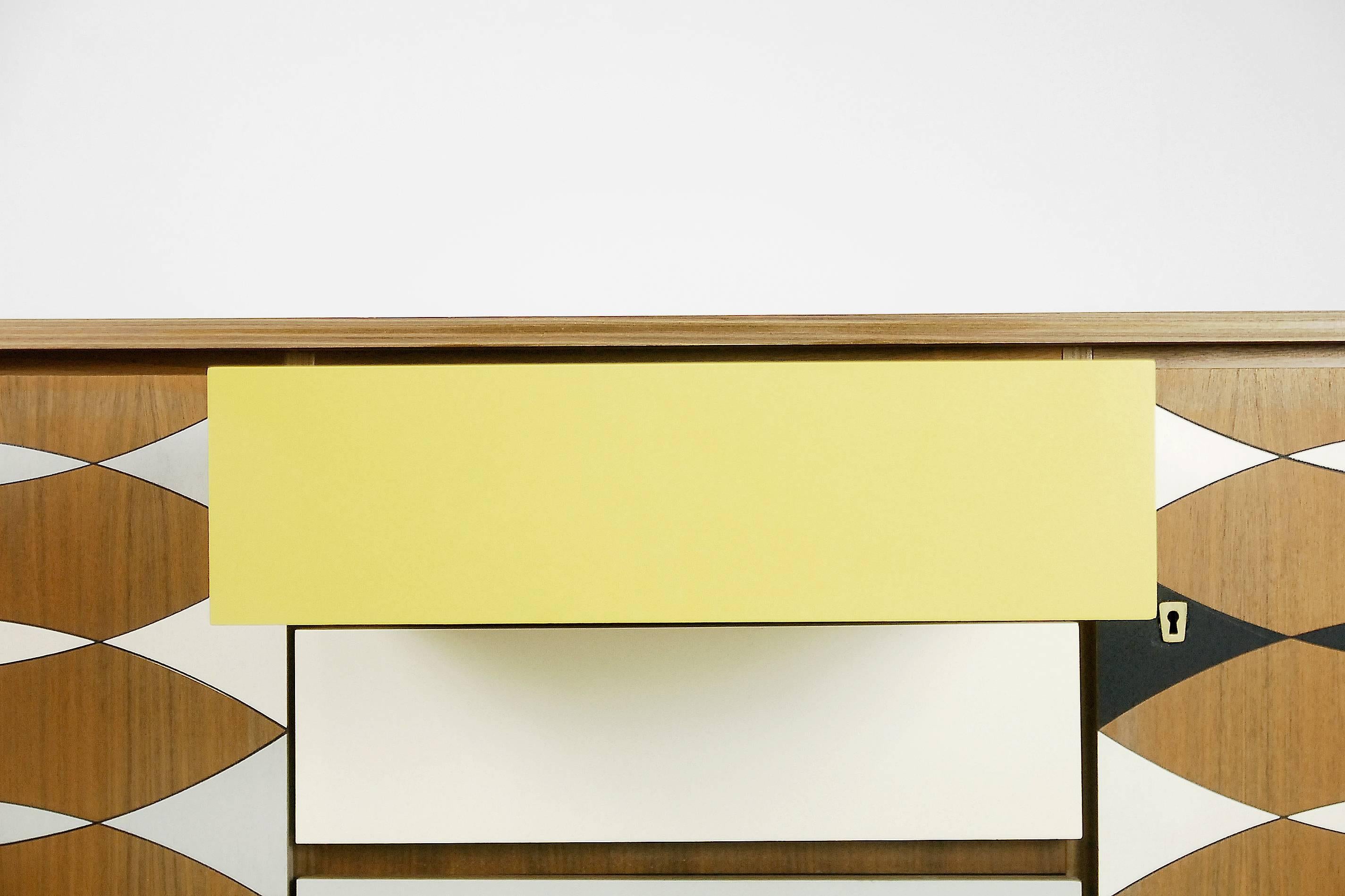 This wide sideboard was manufactured in Sweden during the 1960s. It is made from walnut and wood veneer. The front has been decorated in a hand-painted Scandinavian pattern in yellow, grey and white colors. This sideboard has three doors and three