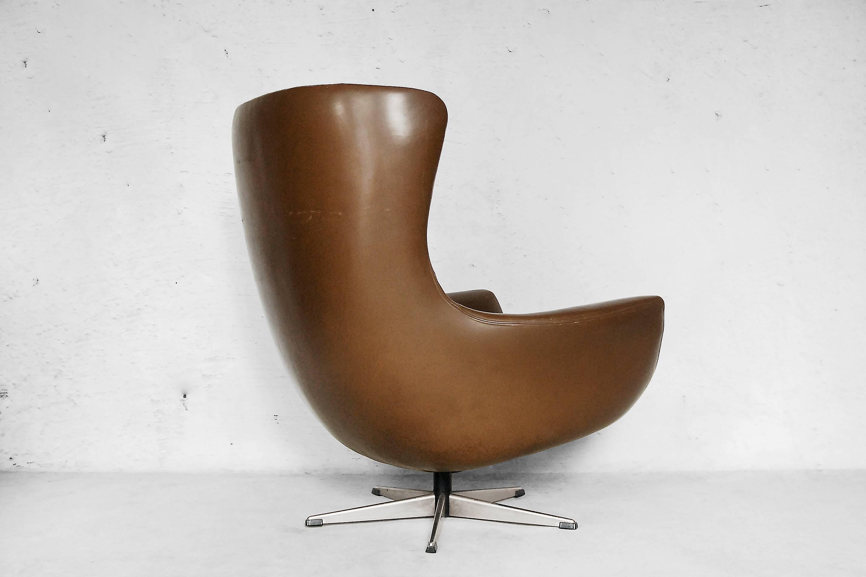 This Mid-Century Modern chair was manufactured in Scandinavia during the 1960s. It has a modern egg form referring to the Space Age style, similar to Arne Jacobsen projects. It is made from varnished leather in a brown color and has a swivel base