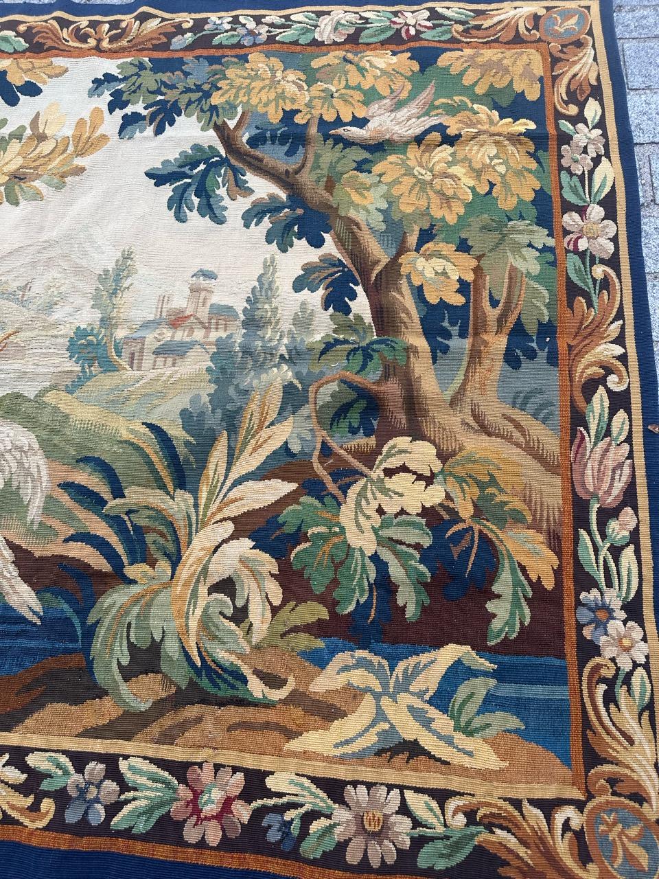 Très belle tapisserie ancienne d'Aubusson représentant une vue de la nature dans les bois, avec des oiseaux, des arbres et une rivière. On aperçoit plus loin des maisons de village. Avec de jolies couleurs naturelles dans les tons de jaune, vert,