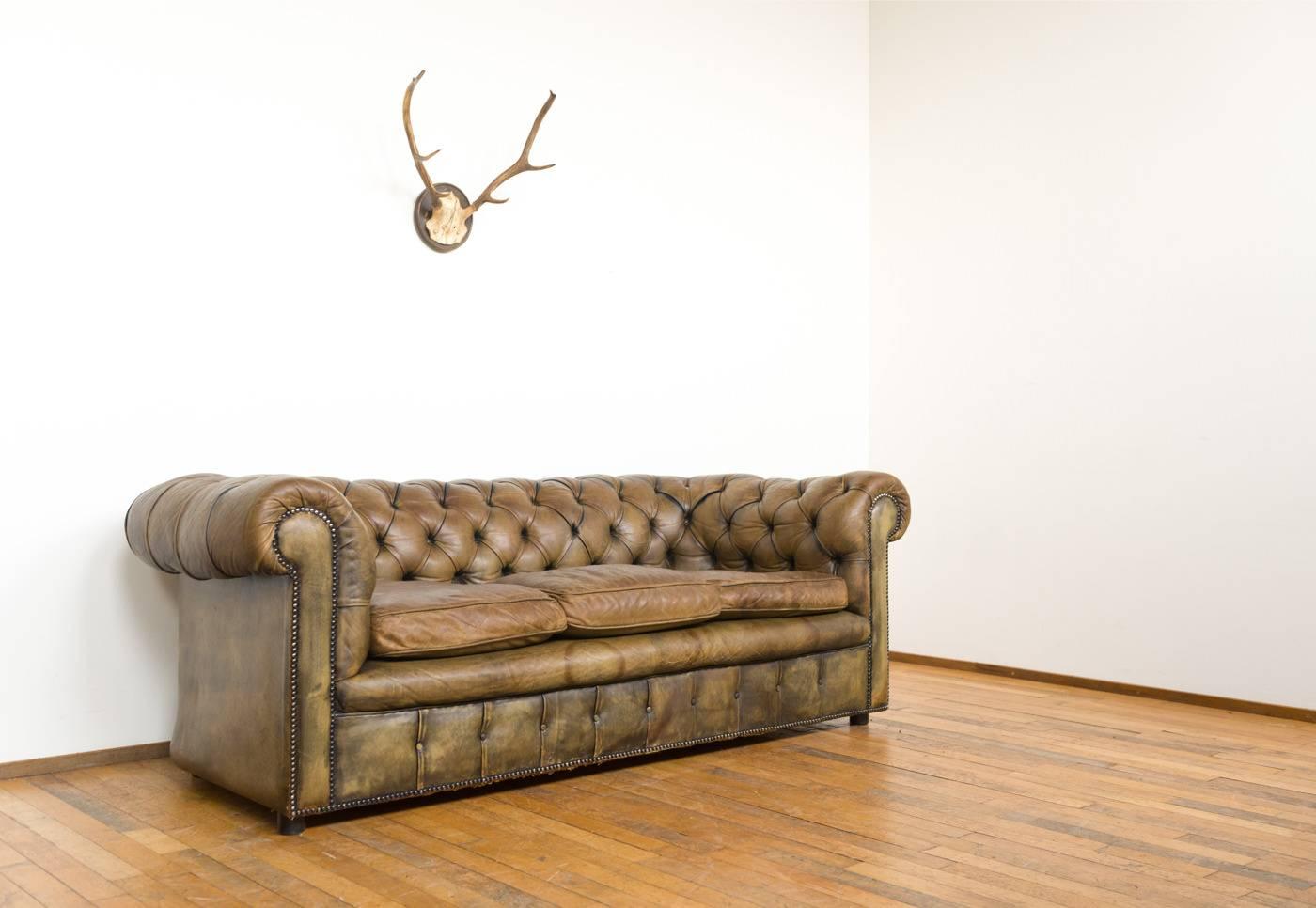 This Chesterfield was made in 1950s/1960s. The leather was hand-dyed which gives the sofa a beautiful gradation of colours, from dark brown in the folds to an olive green color on lighter places. The leather has gotten a beautiful patina over the