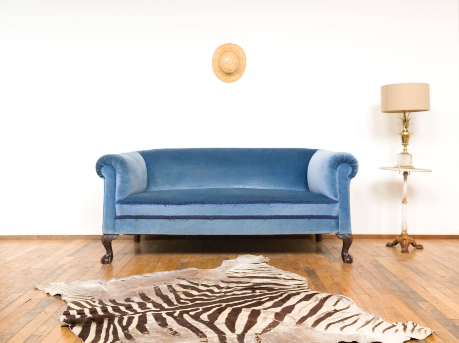 This elegant sofa dates from the early 20th century and has been fully restored and reupholstered in a beautiful, blue velvet. The sofa is mounted on detailed ball- and claw feet made out of mahogany.