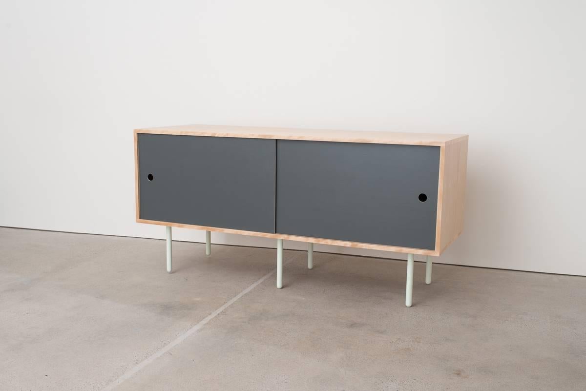 Basic Bitch is a simple box credenza made from Birch plywood and powder coated steel legs. The sliders can be interchanged or customized and are shown in white, gray, or quartz laminate, and also in bronze mirror acrylic. A classic but simple design