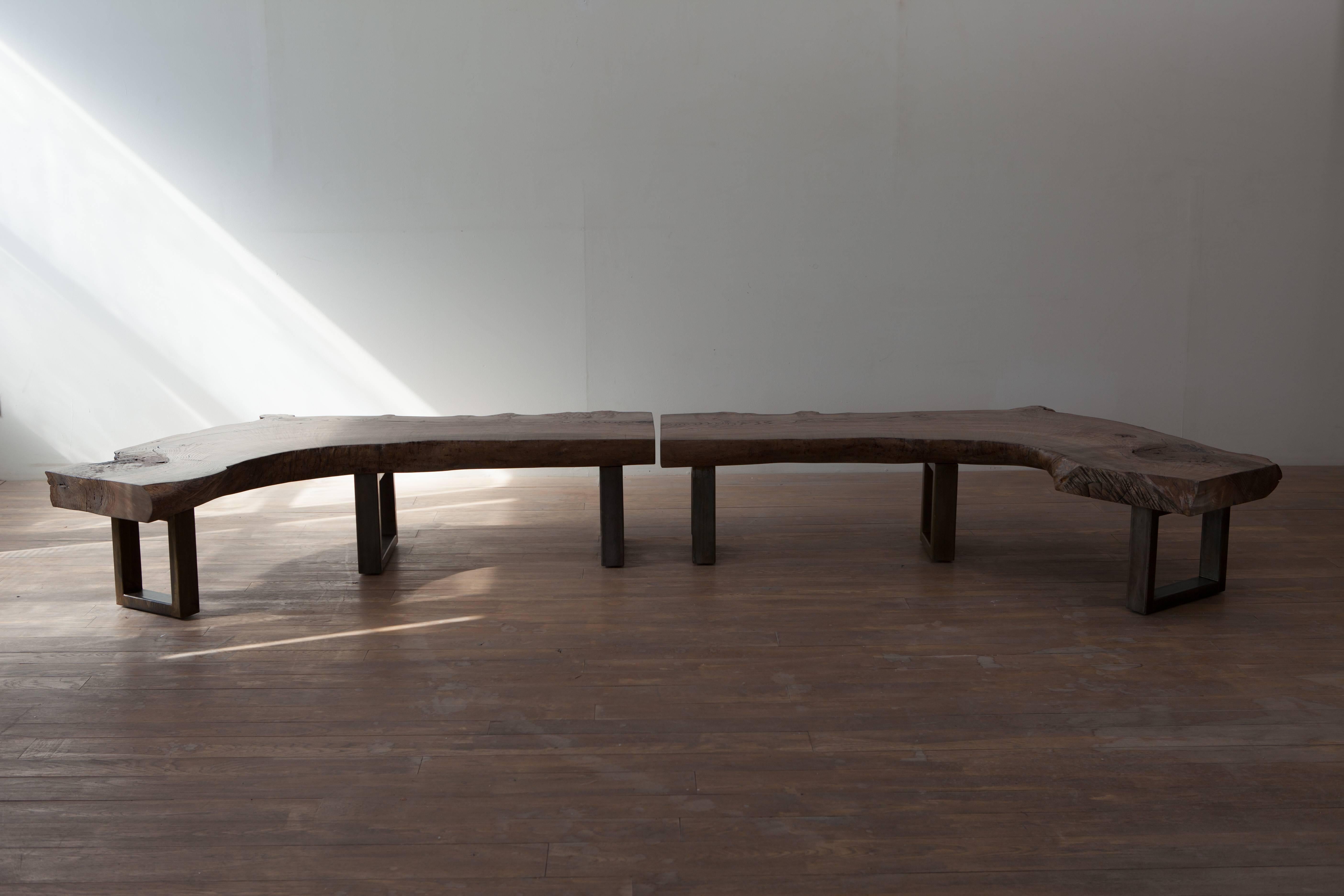 Two mirror image curved benches permitting right and left seating in front of a fire place or a corner of a room. 
Can be purchased as a set or individual bench. The combination of reclaimed ash with bronzed steel legs creates a minimal and warm