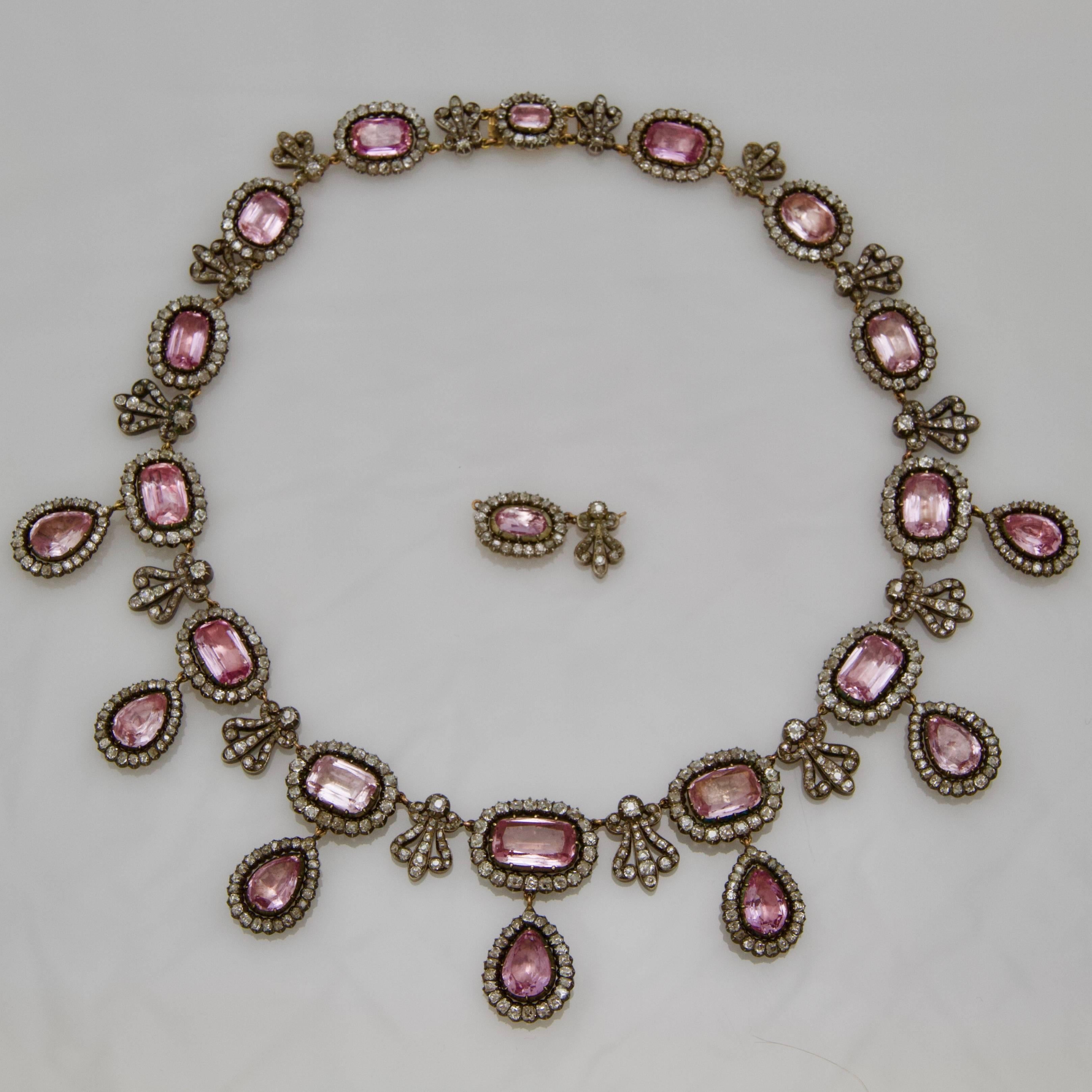 An antique and rare pink topaz and diamond, gold and silver necklace in its red leather case.
Front set with 14 faceted rectangular pink topaz framed by antique-cut diamonds alternating with diamonds palmettes and supporting seven pear-shaped pink