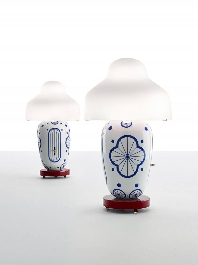 Chinoz Ming is a table lamp featuring a white ceramic body with hand-painted, orient-inspired ornaments. The polished brass dimmer runs along a vertical groove in the ceramics body. A carefully selected burgundy color of the lacquered wooden base