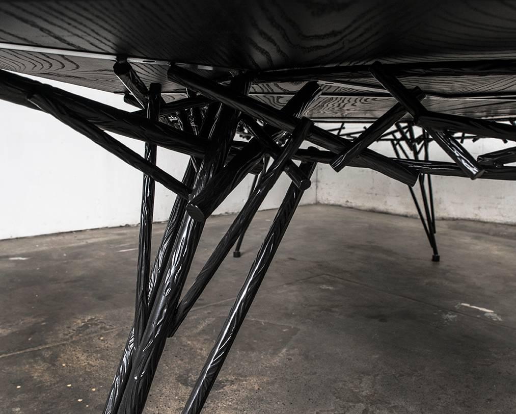 Modern ebonized hardwood and powder coated steel dining table. This modern table is an exploration with ornamental steel and the chaos found within the woven branches of a birds nest. Shown with a solid ebonized white ash top and a blackened steel