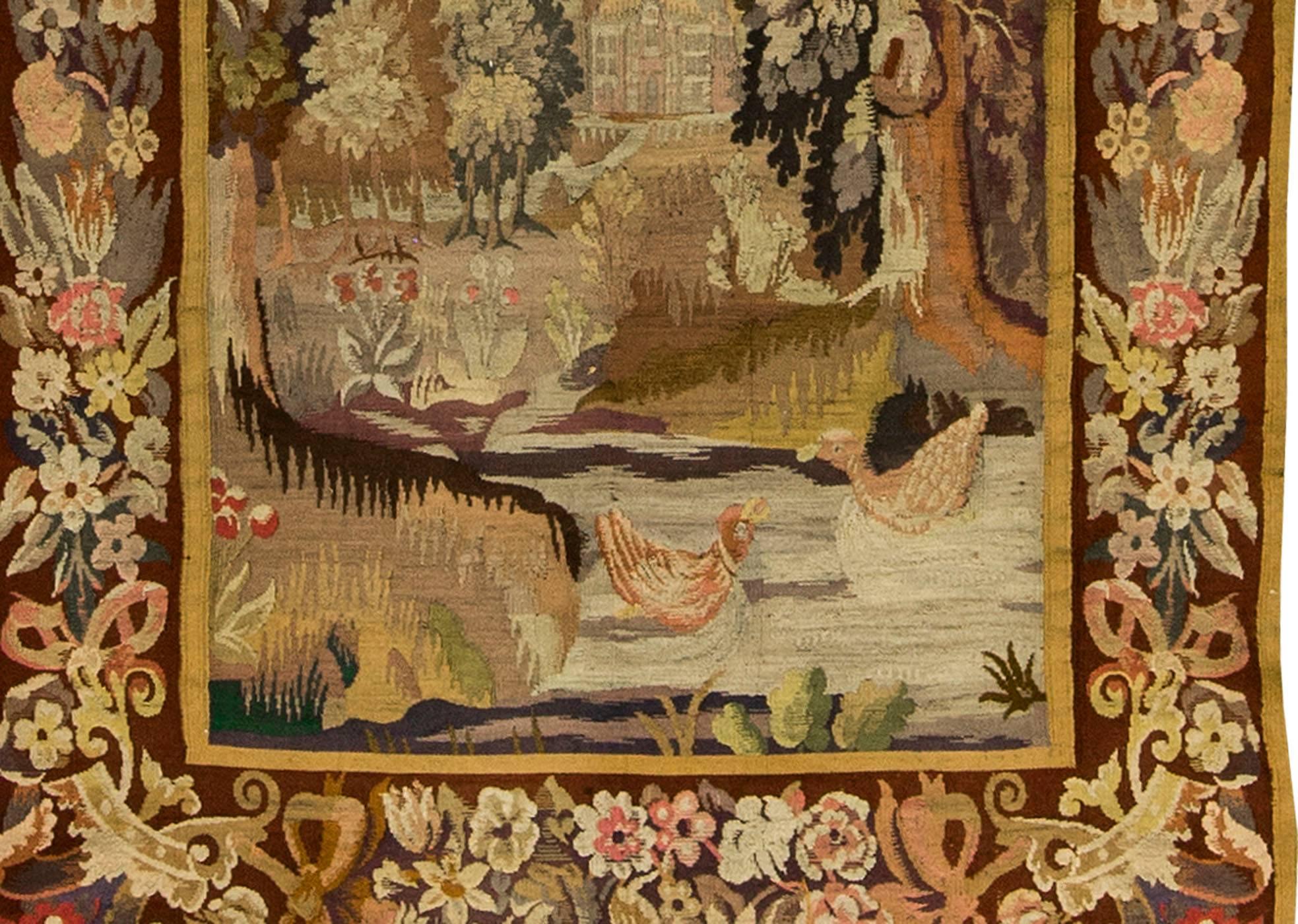 19th century French tapestry. A countryside scene with a stream running down to the large country houses in the background. A pair of birds are playing in the water with overhanging trees dense with foliage.
