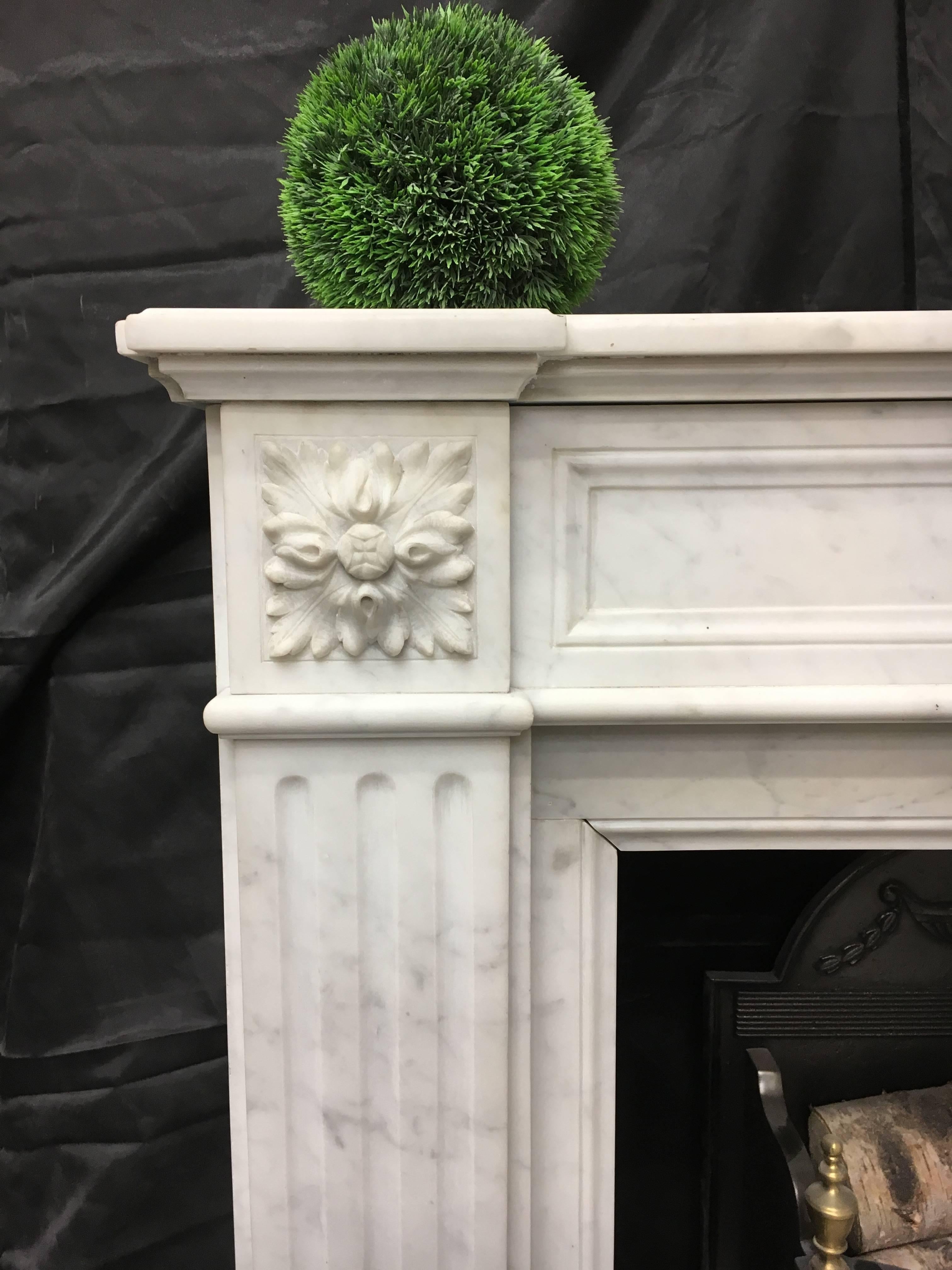 A fantastic example of a French Carrara marble fireplace, displaying excellent carving. An elegant sunflower is centered in the frieze flanked by recessed panels with square Patrae to capitols. Jamb returns have a recessed border. A small and