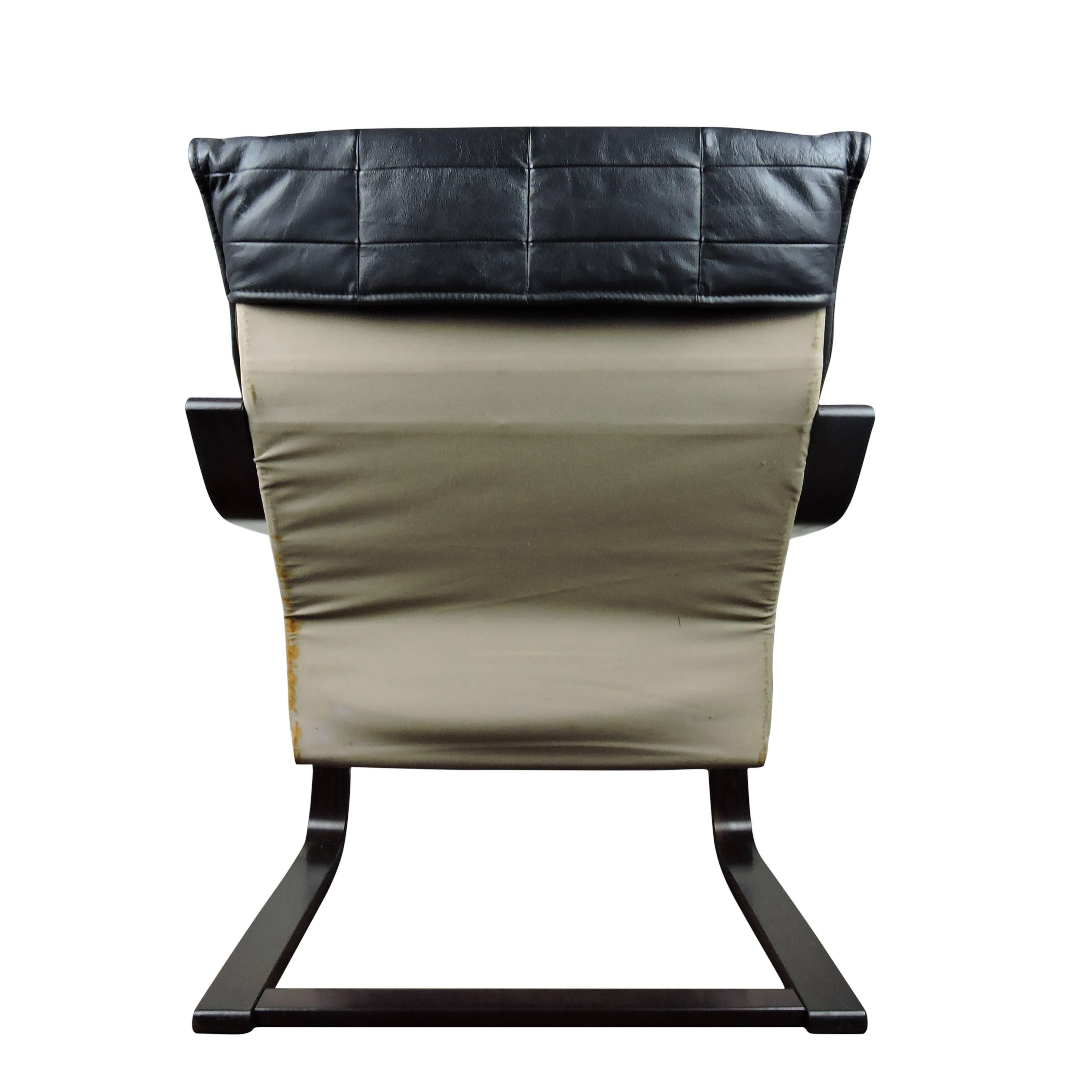 A Danish cantilever chair with stained pre-formed laminate frame featuring a black leather seat covering.