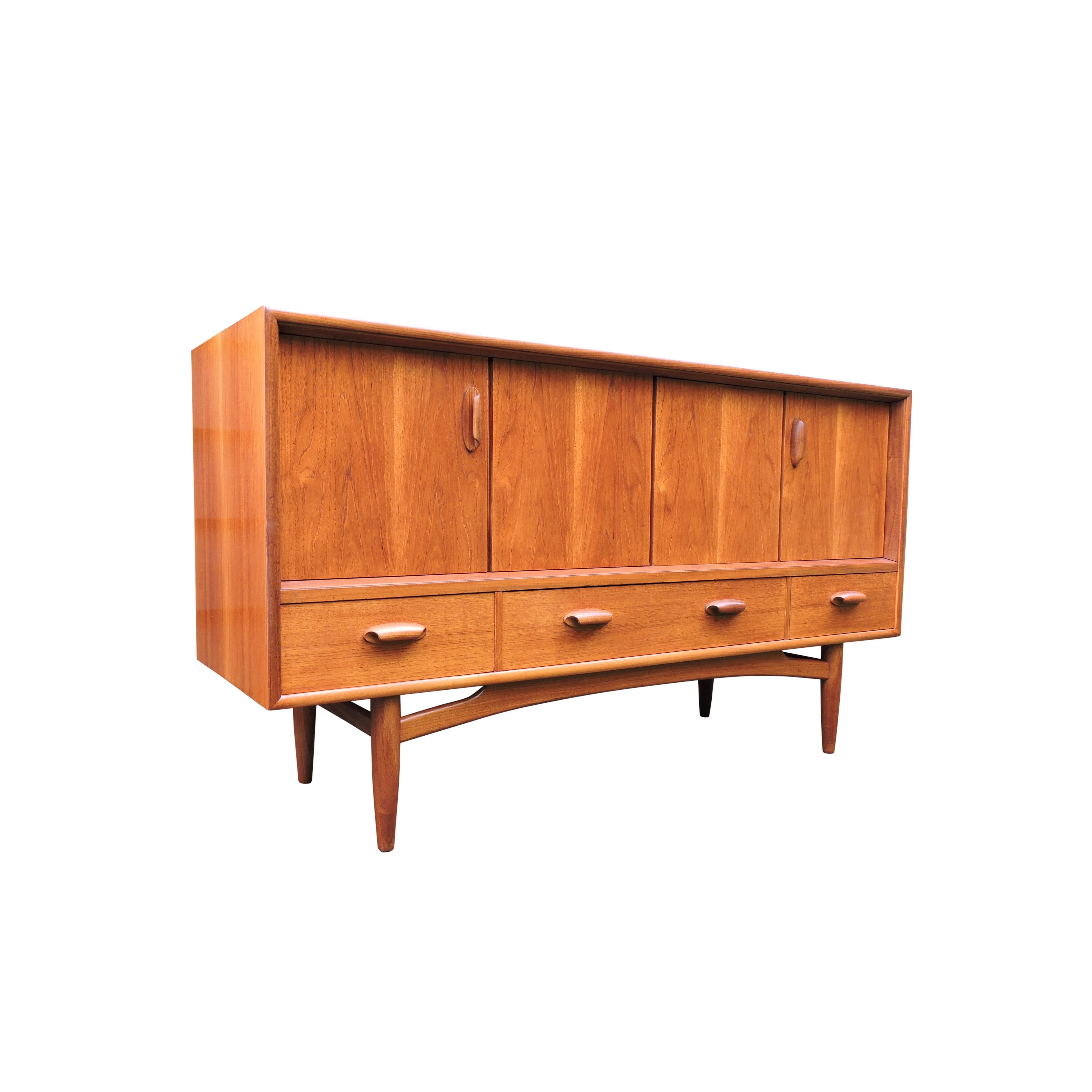 A midcentury teak sideboard from G-Plan featuring three drawers to the bottom and two large cupboards above with bi-fold doors. The doors open with solid teak curved handles and the unit sits on a solid teak frame.
    