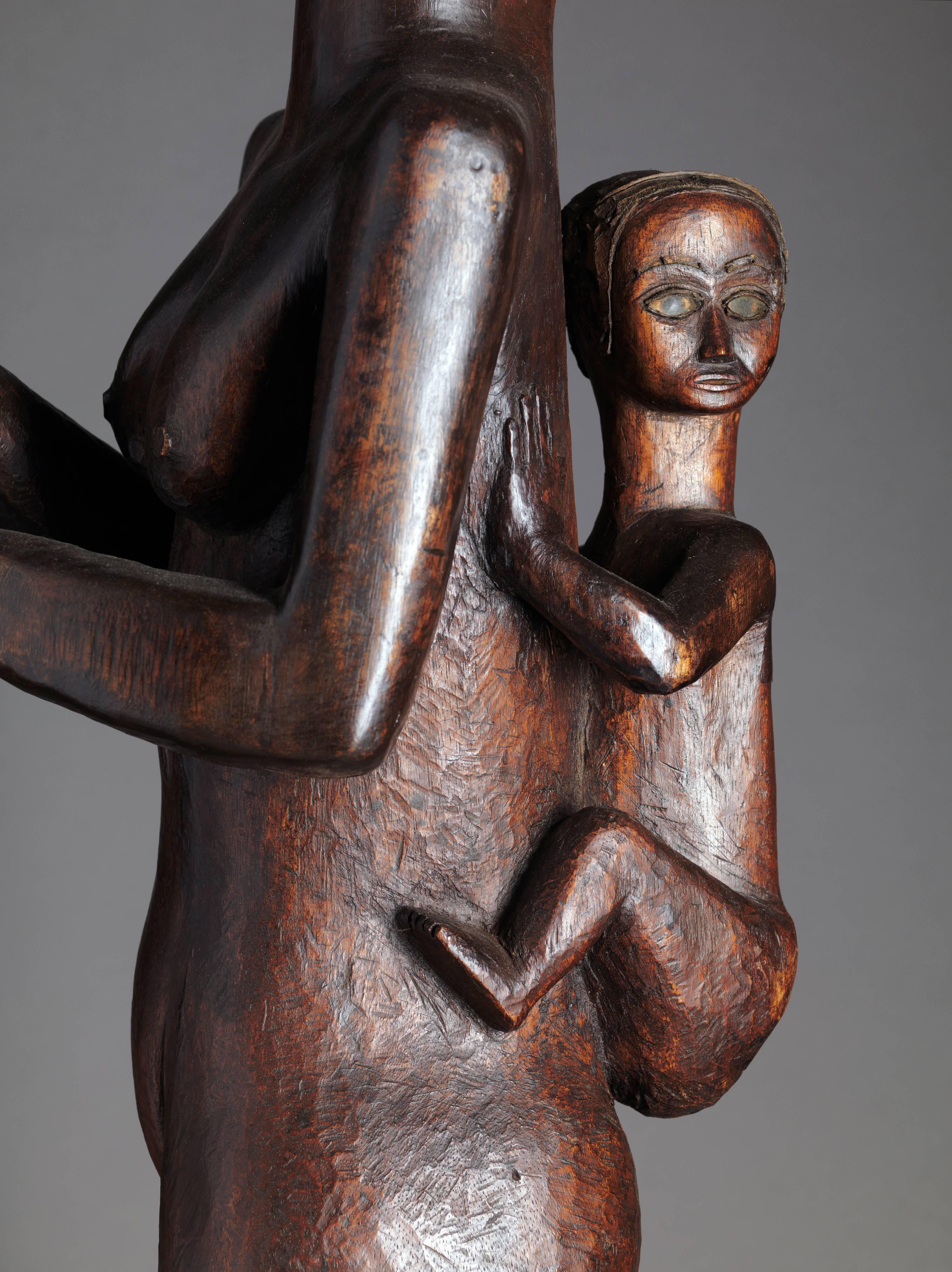 Standing Fang Mabea Maternity of Museum quality, holding a pestle with both her hands. The mother's head is slightly turned to the left, while the child, which she carries on her back, has his head turned to the right. Her left leg indicates a