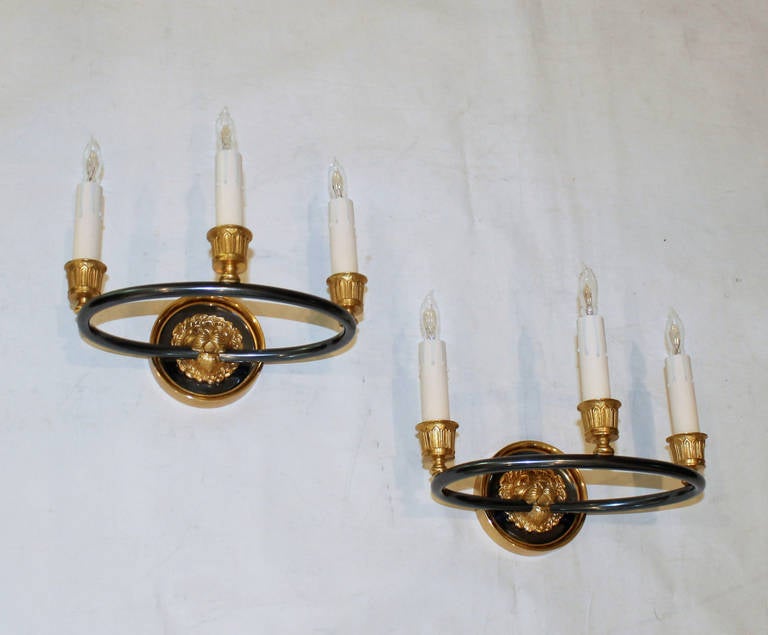 Pair of beautifully detailed pair of doré bronze Empire style walls sconces by Maison Bagues, Paris. Bagues style #17809. Lion motif to backplate with 3 candle cups in gilt and gun metal finish. Newly wired for US, each sconce uses 3 B or candelabra