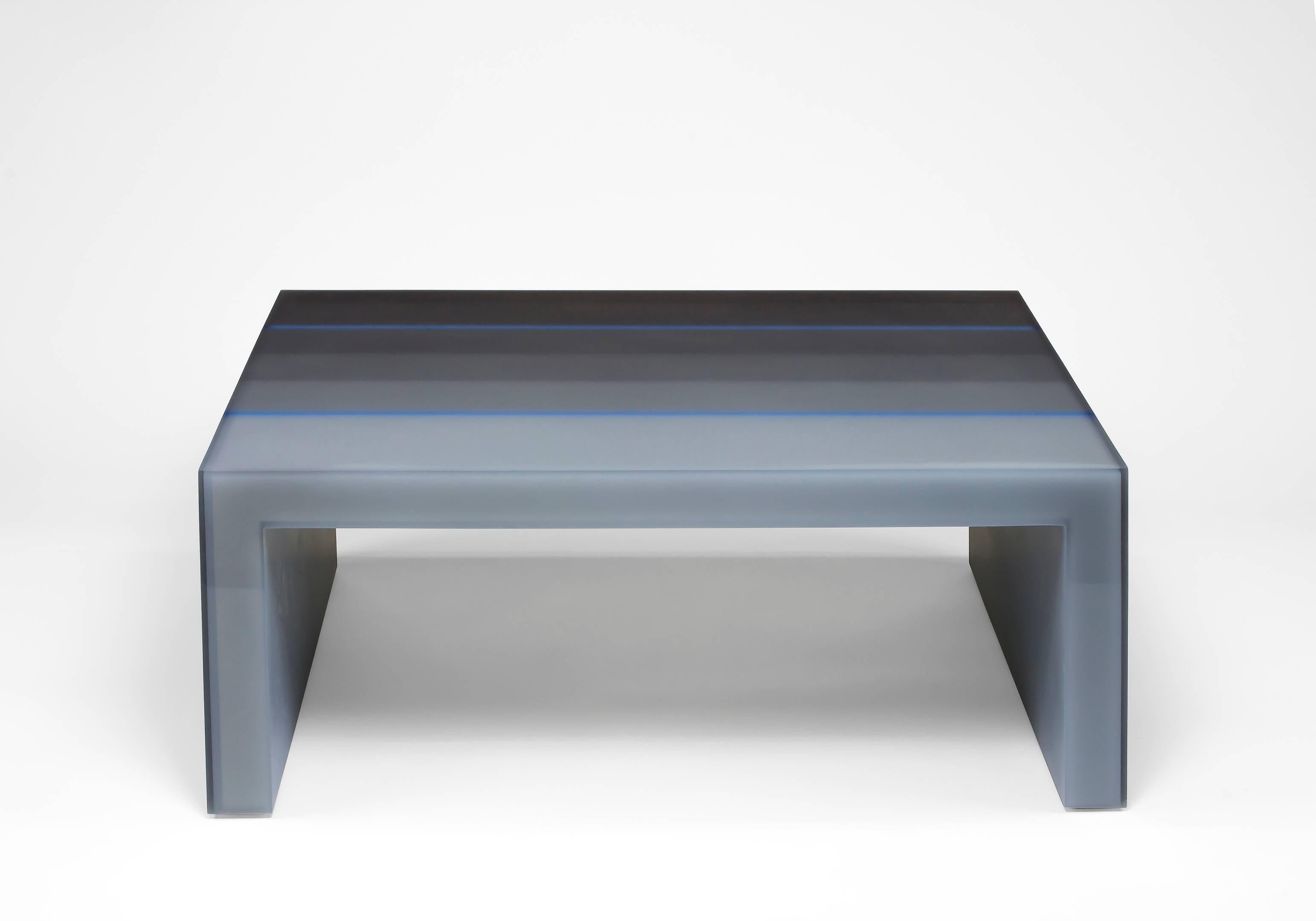 This coffee table uses Facture Studio's gradient style to transition in six layers from a deep opaque to water clear gray over a light gray resin core. Two water clear blue lines disrupt the gradient and contrast the their opacity. The interior and