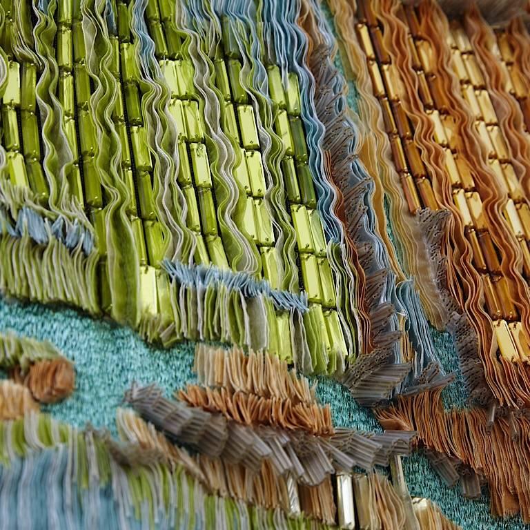 Hand embroidered wall hanging designed and made by Geraldine Larkin.
Olive,aqua,ochre,lime,light amethyst and ivory shades are used to embroider this subtly lustrous textile.
Light plays on and reflects from the mosaic mirrors and beads in a myriad