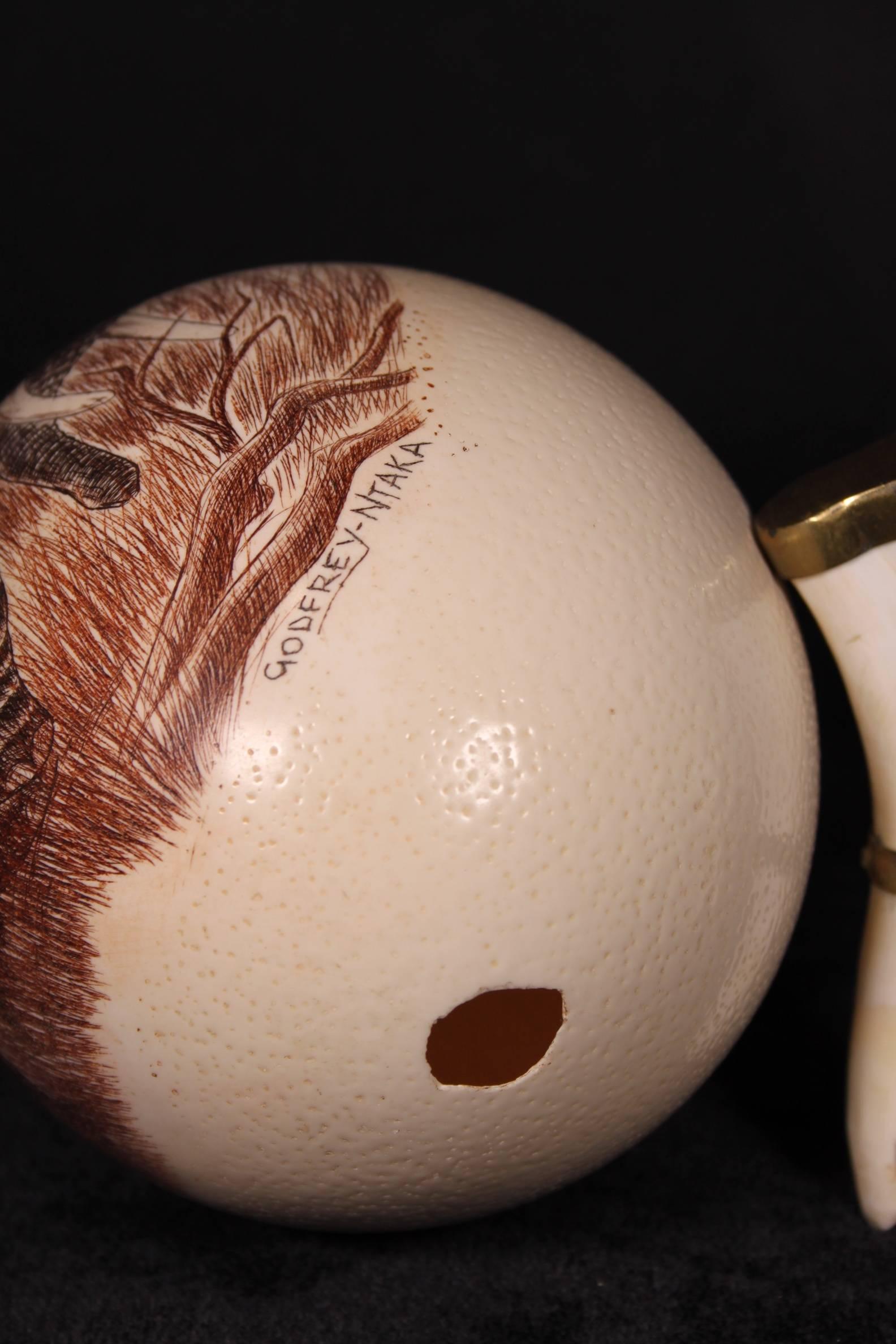 20th Century Ostrich Egg African Art signed carving. Signed Godfrey Ntaka on a tooth and brass mount. 