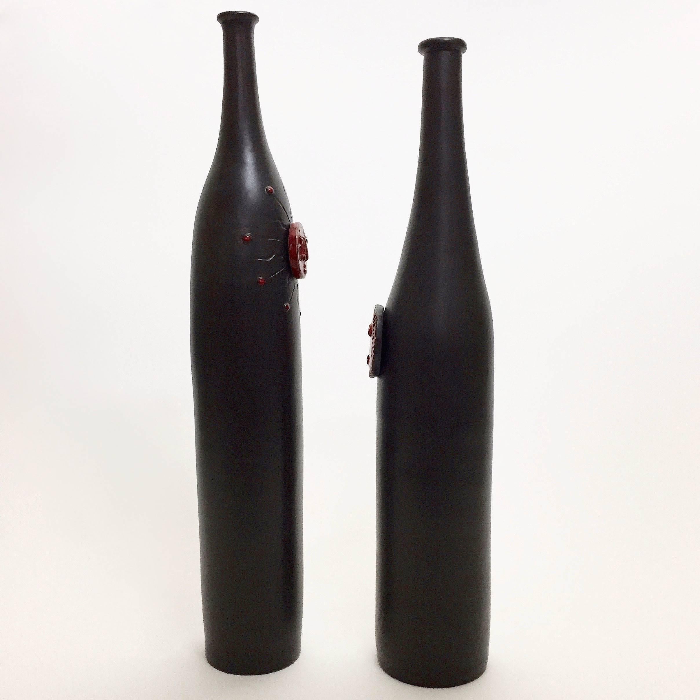 Pair of ceramic vases, bottle shaped, glazed in matte black and decorated with glossy red biomorphic medallions in front.
One of a kind handmade pieces signed by the French ceramicists, the DaLo.

Dimensions approx. are:
- Large: H 47.5 cm, D 7
