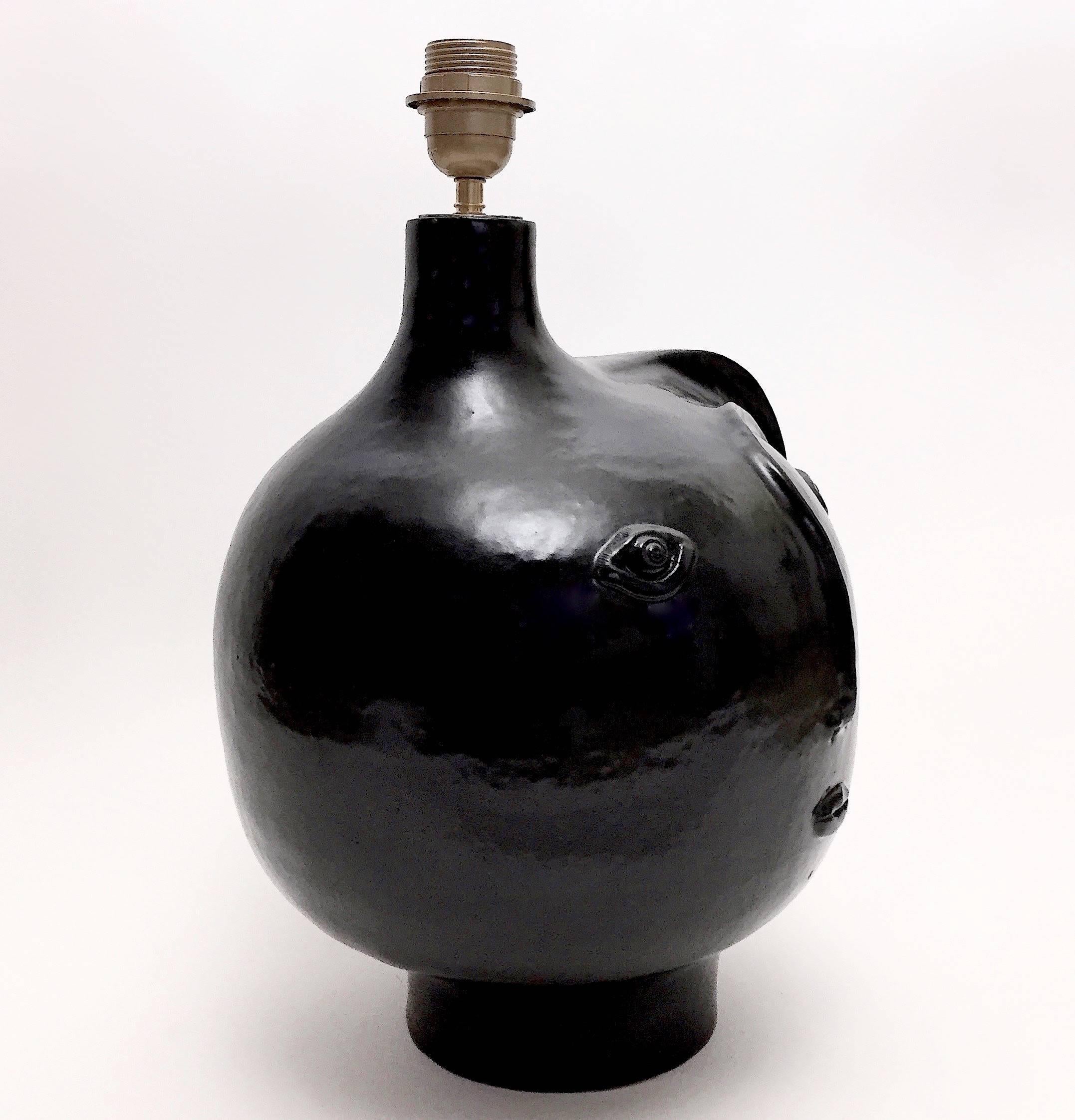 Handmade biomorphic sculpture forming lamp-base.
Stoneware glazed in glossy black, decorated with stylized visage sculpted in front.
One of a kind ceramic piece designed and signed by the French ceramicists, Dalo. 

The height measurement is for