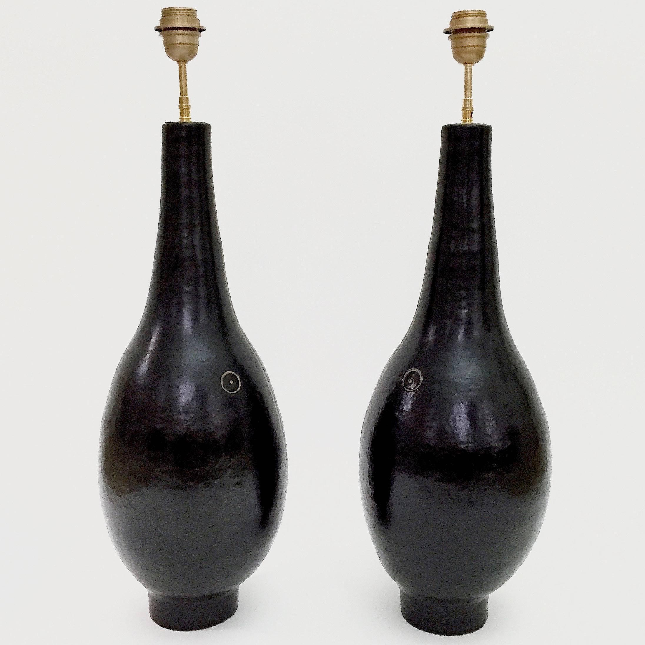 Important pair of lamp bases, bottle shaped, stoneware glazed in glossy black, decorated with stylized visages engraved in front. 

Unique handmade pieces designed and signed by the French artists, Dalo. 

The height dimensions approx. are