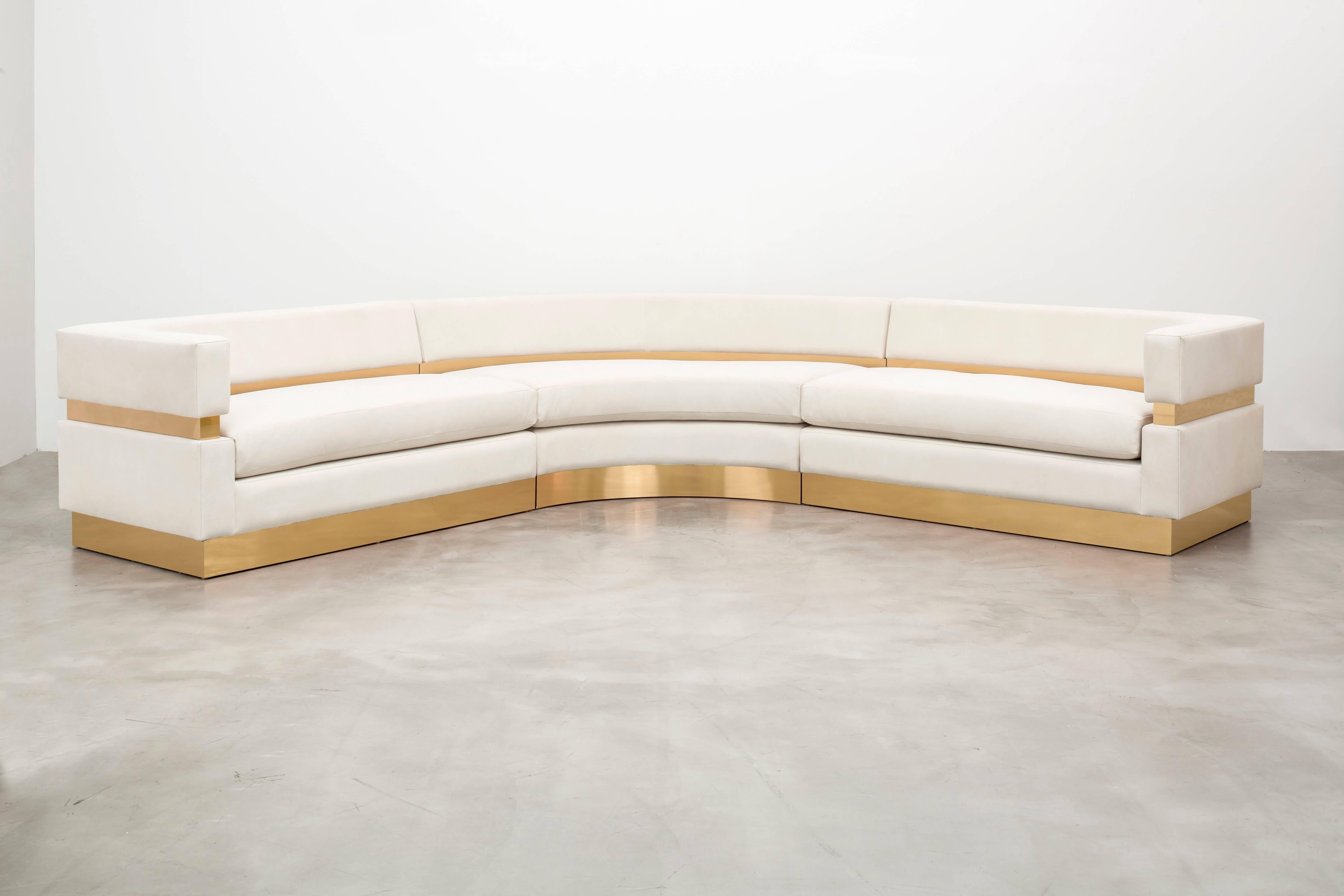 The Cardin sectional sofa features layers of upholstery and metal inlay to create a minimal and modern sitting statement. This is a showroom sample sold as is. As shown in Ivory Leather with Polished brass inlay.