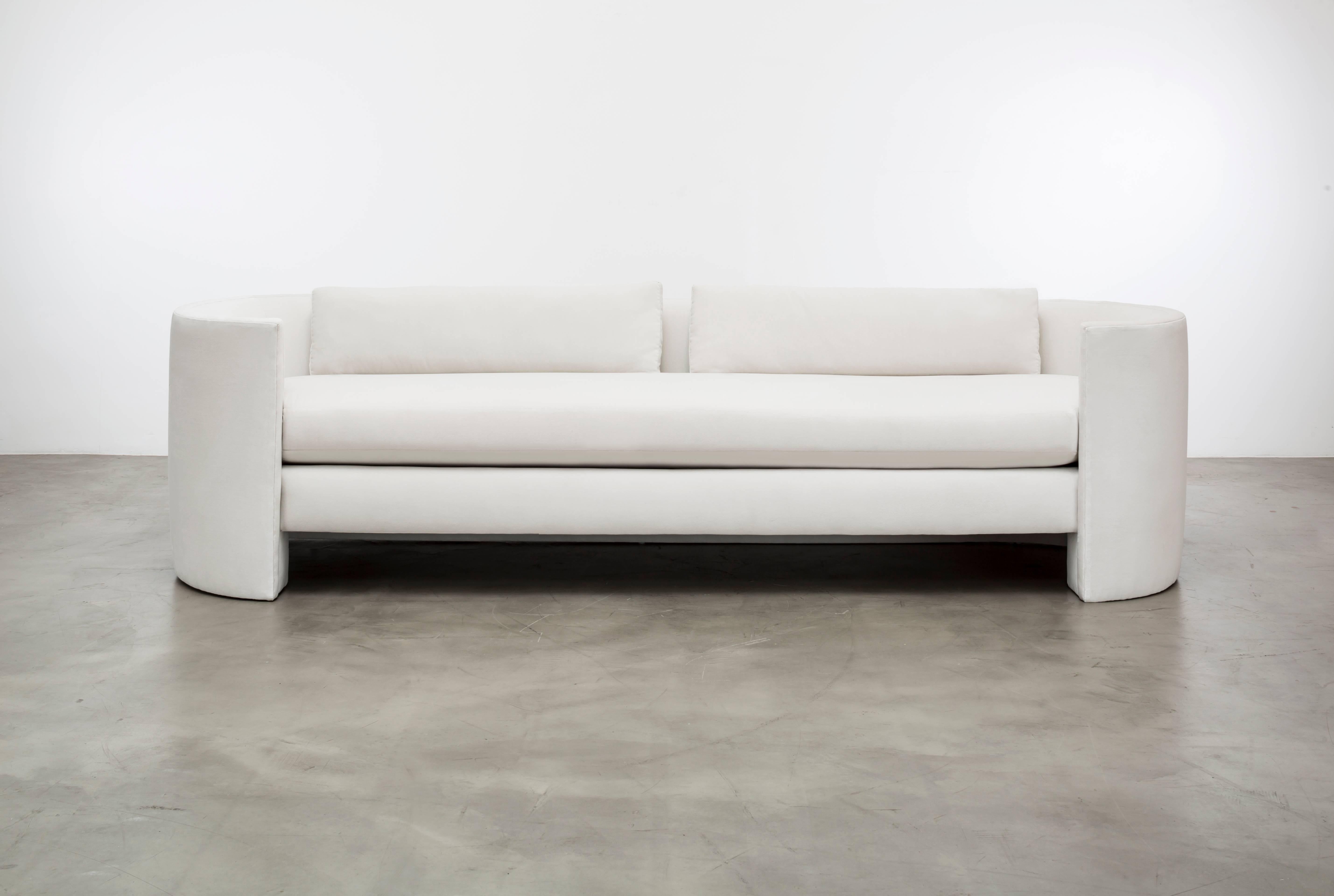 The Claire sofa features an upholstered hovering plinth cushion seat and a back waterfalls to the floor. This is a showroom sample sold as is. As shown in a cotton velvet white.