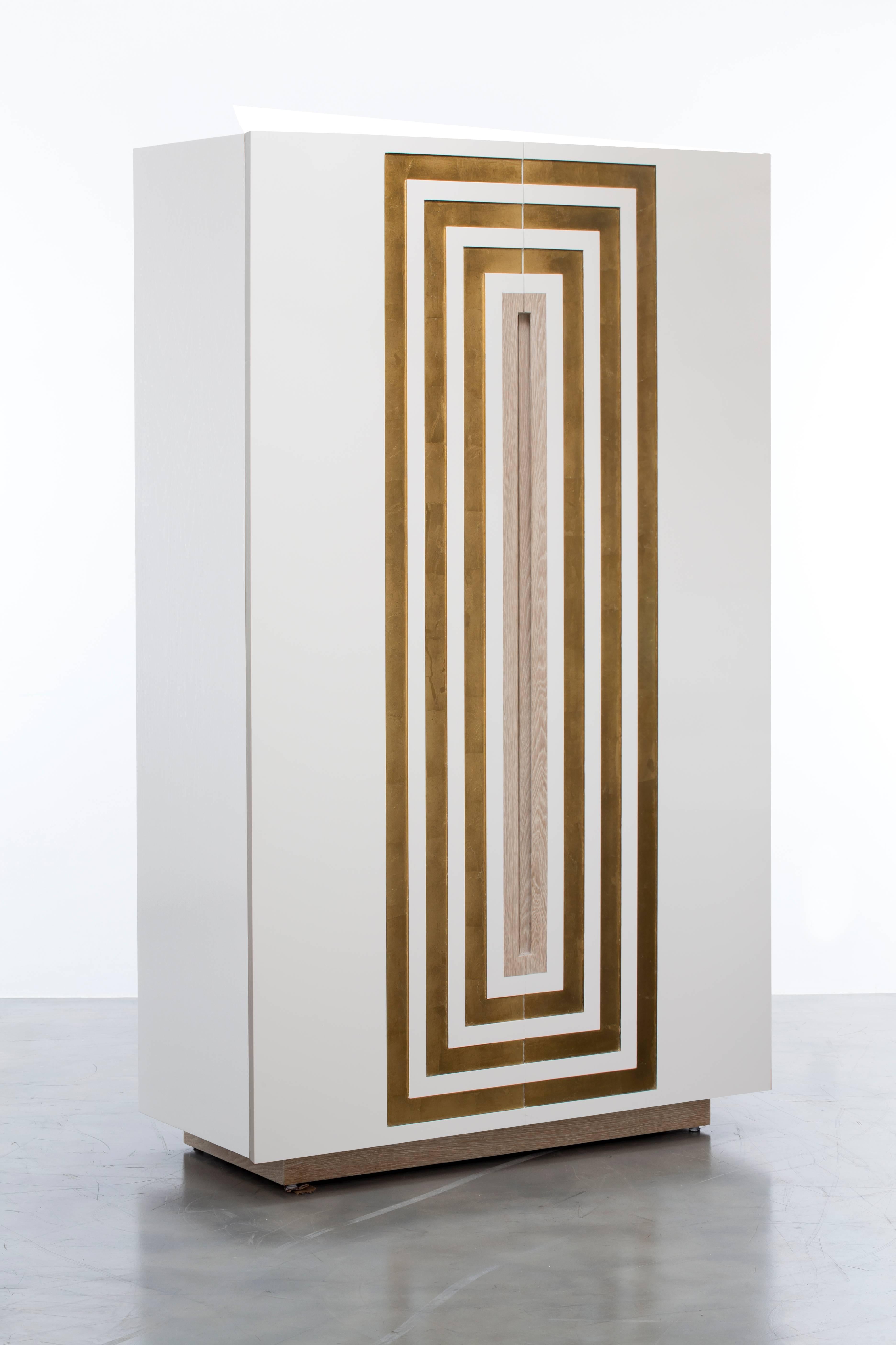 The Celeste bar cabinet features a white lacquer over oak body with a gold leaf inlay detail. The interior standard comes as a dry bar including puck lighting, Carrara marble, four drawers and liquor bottle storage.  This is a showroom sample sold