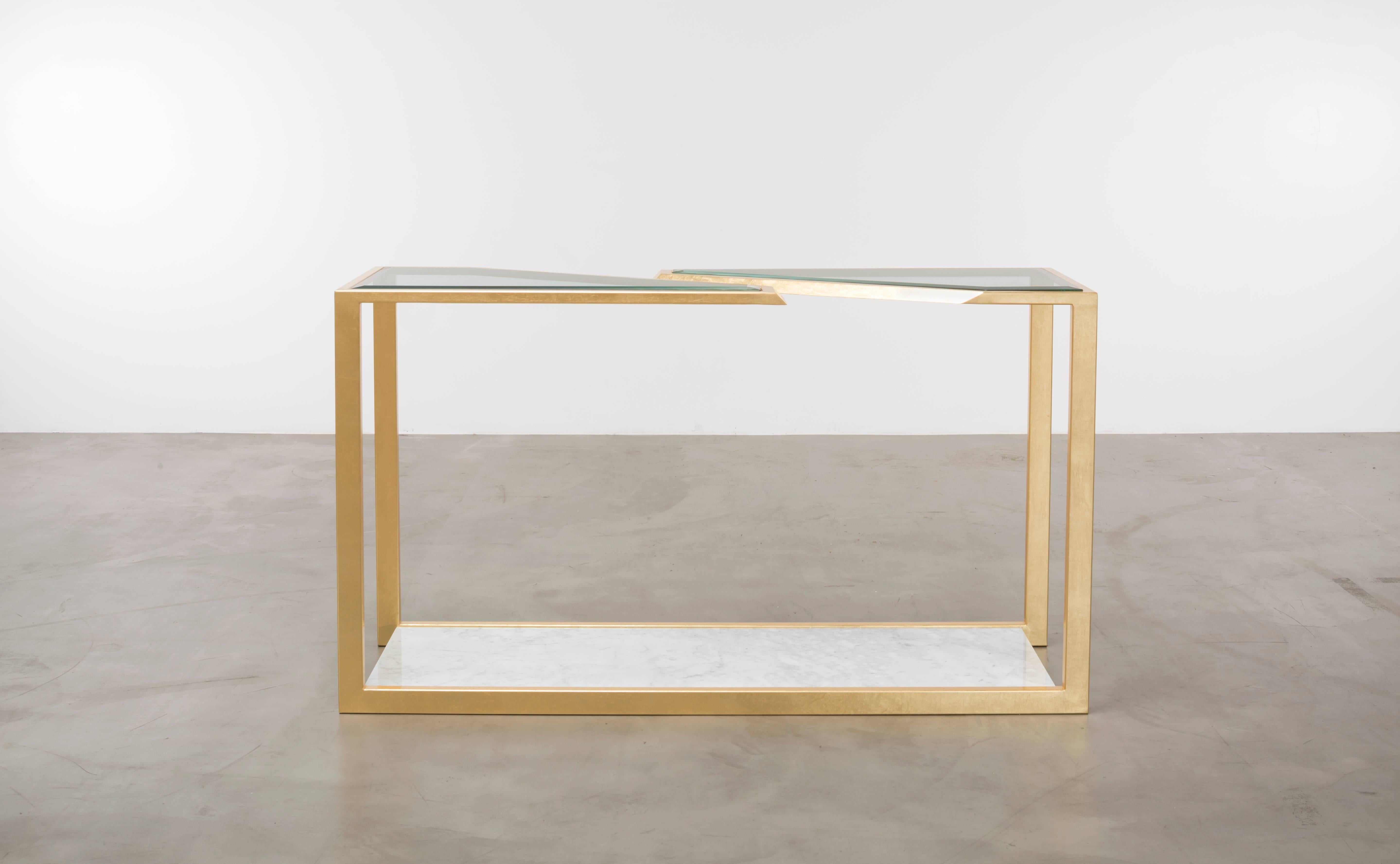 The Pierre console table is a modern fractured gold leaf console table made of gold leaf over iron with Carrara marble and bevelled edge glass. This is a showroom sample sold as is.
