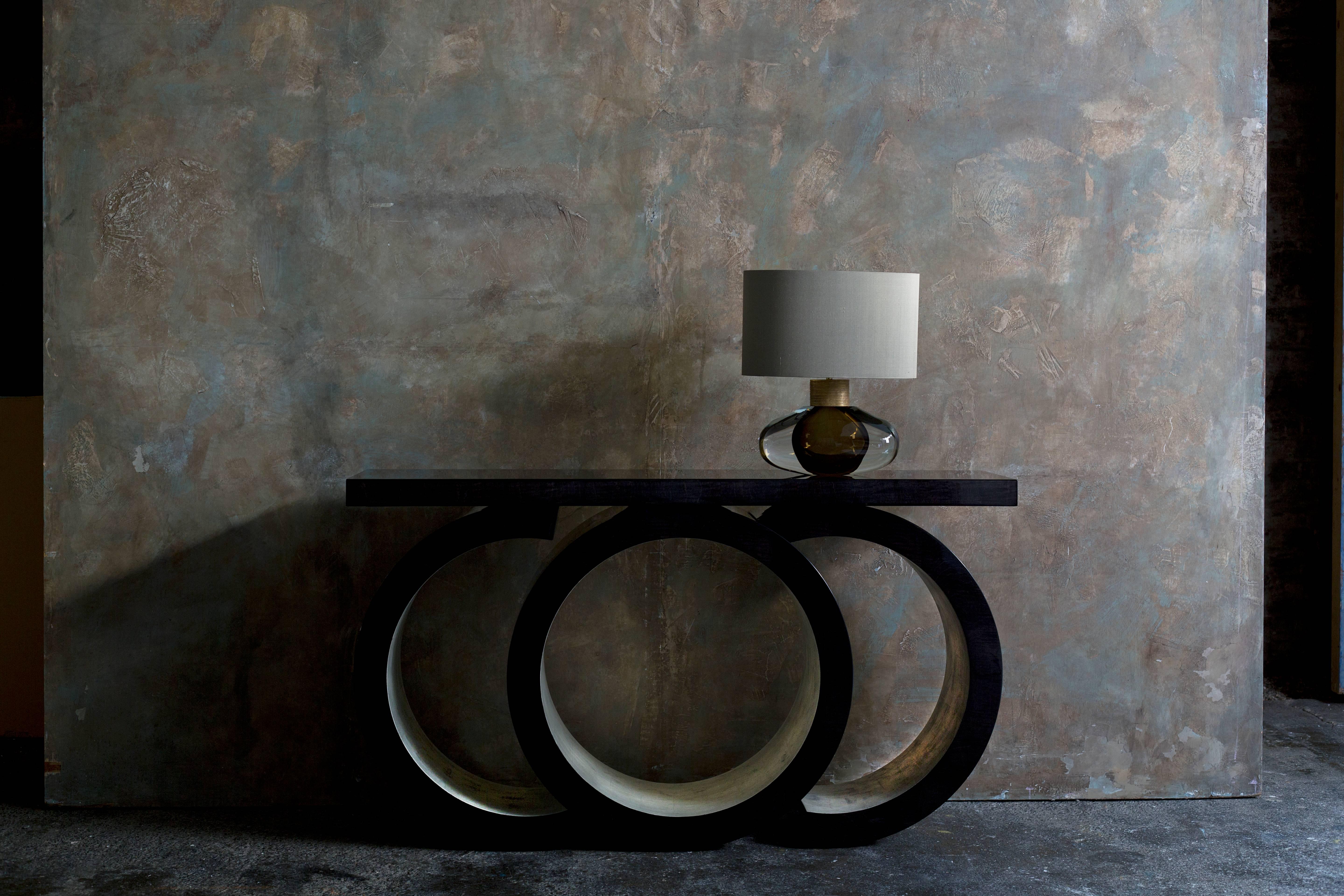 A magnificent console table finished in high sycamore black and white gold leaf.

With its unique pedestal formed of two elegant arcs surrounding a defiant central cylinder, this extraordinary piece will transform any room by its sheer presence and