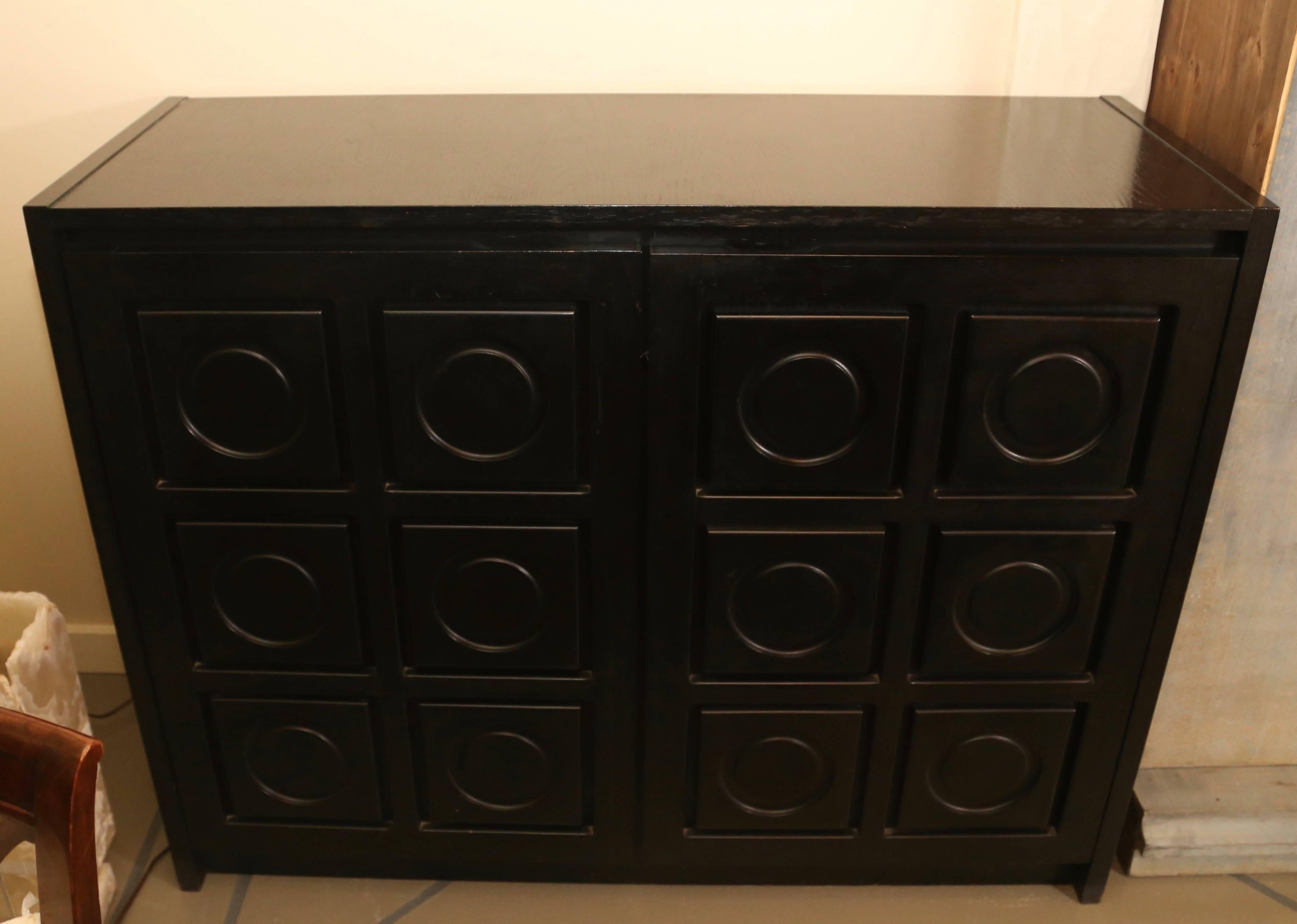 Two-door midcentury cabinet in ebonized oak, with circular motifs carved into the door panels.

Stained oak interior with shelves and drawers. Recessed finger pulls on tops of doors.
  