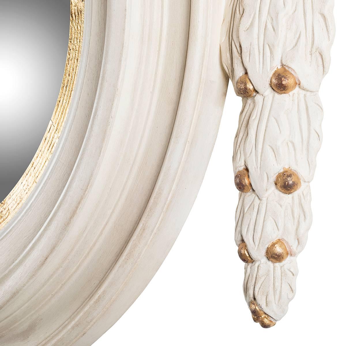 Large round wooden mirror with garland.
This sophisticated mirror is a perfect example of elegance. The round sectioned shape is adorned by a likely carved garland. The finish white with gold details give to this creation an additional touch of