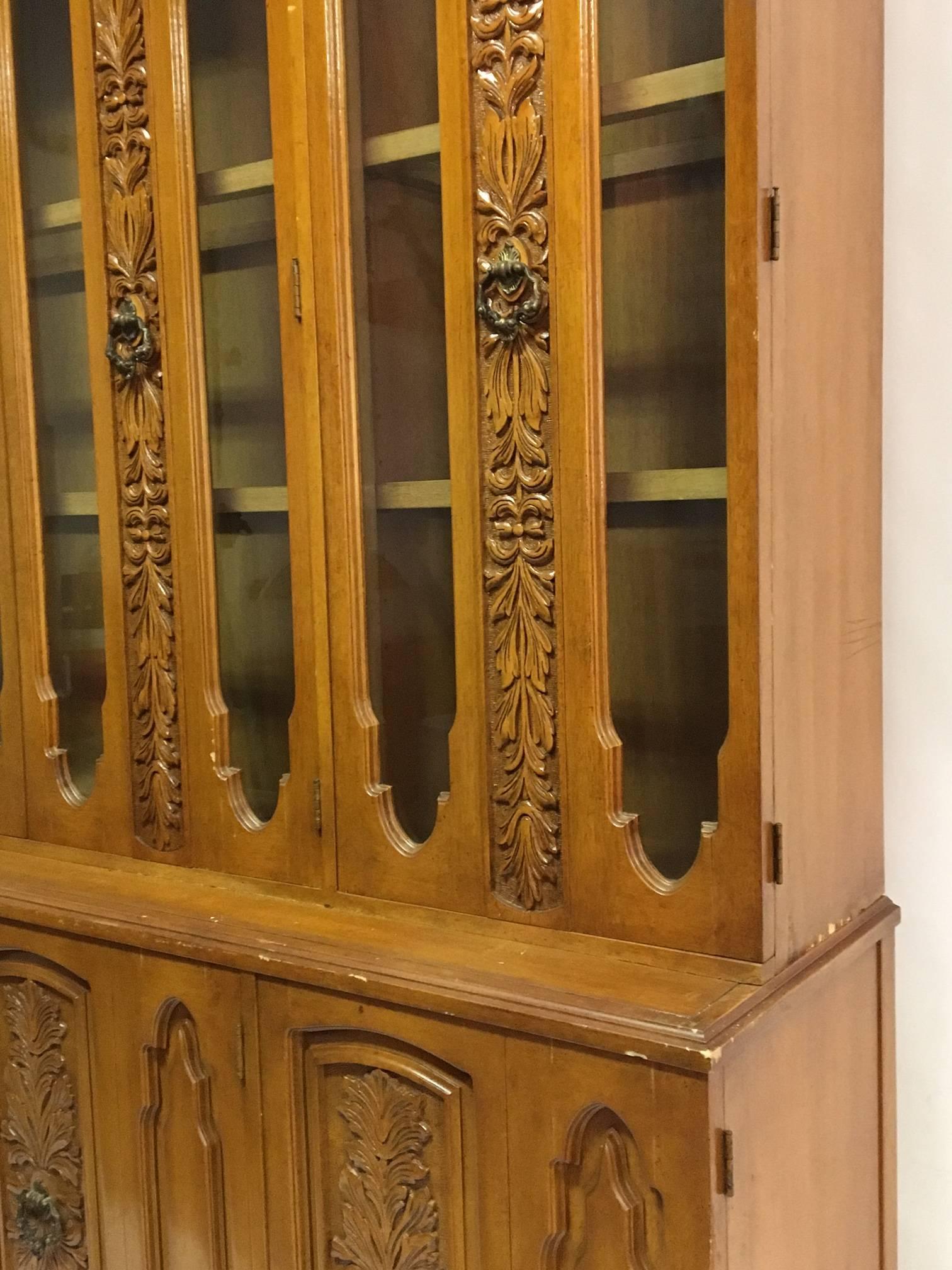 Monumental mid-century china cabinet. Beautiful ornately carved detail surrounds the front glass doors. 
Top hutch features interior lights and glass shelves for display. Lower credenza or sideboard features interior drawers and shelves.
Good