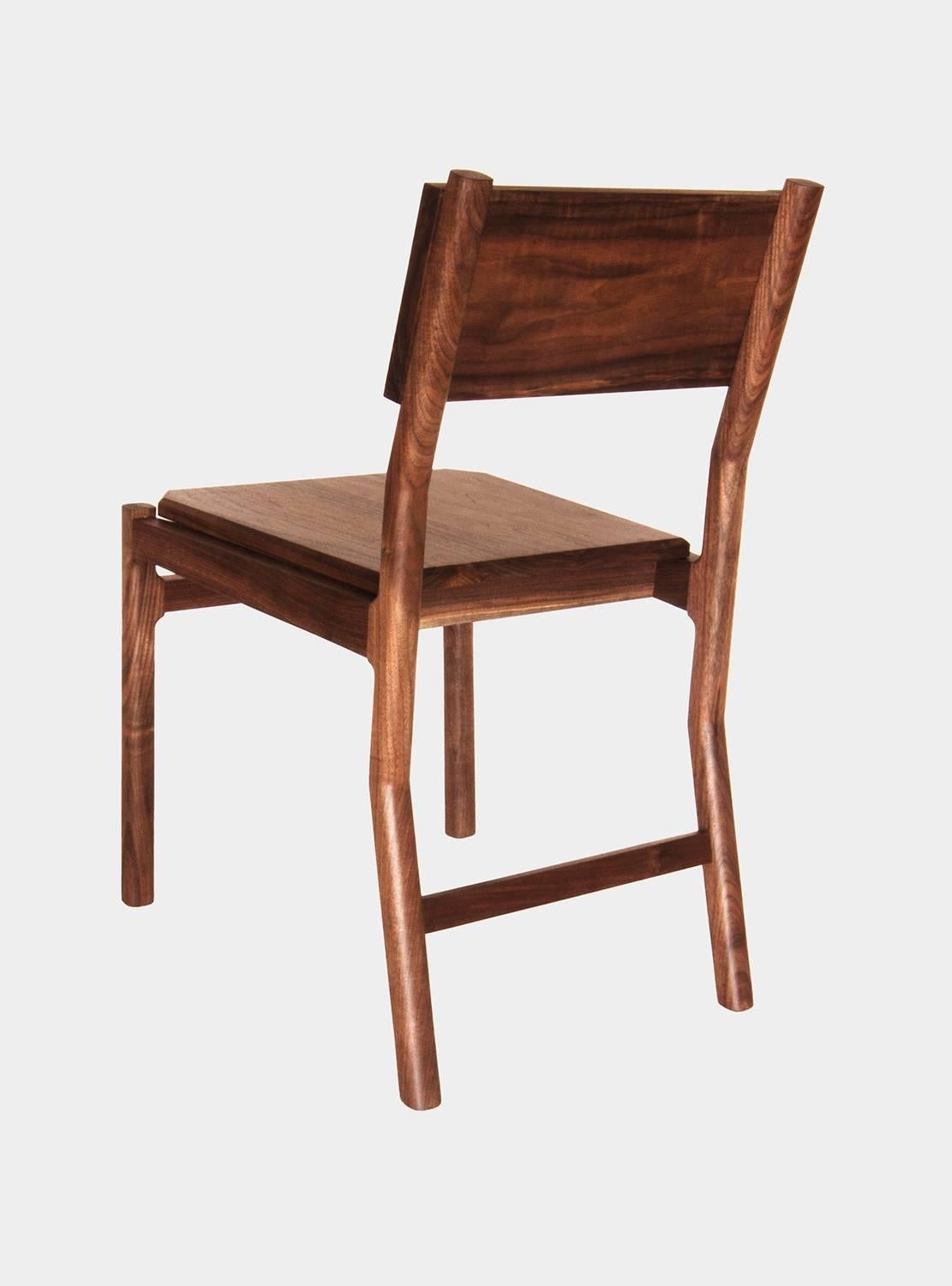 New York Heartwoods' contemporary black walnut Hewitt Dining Chair is influenced by Mid-century Modern and Shaker design, is fabricated for comfort, and features refined joinery, a hand-shaped backrest, faceted seat, and NYH's signature teardrop