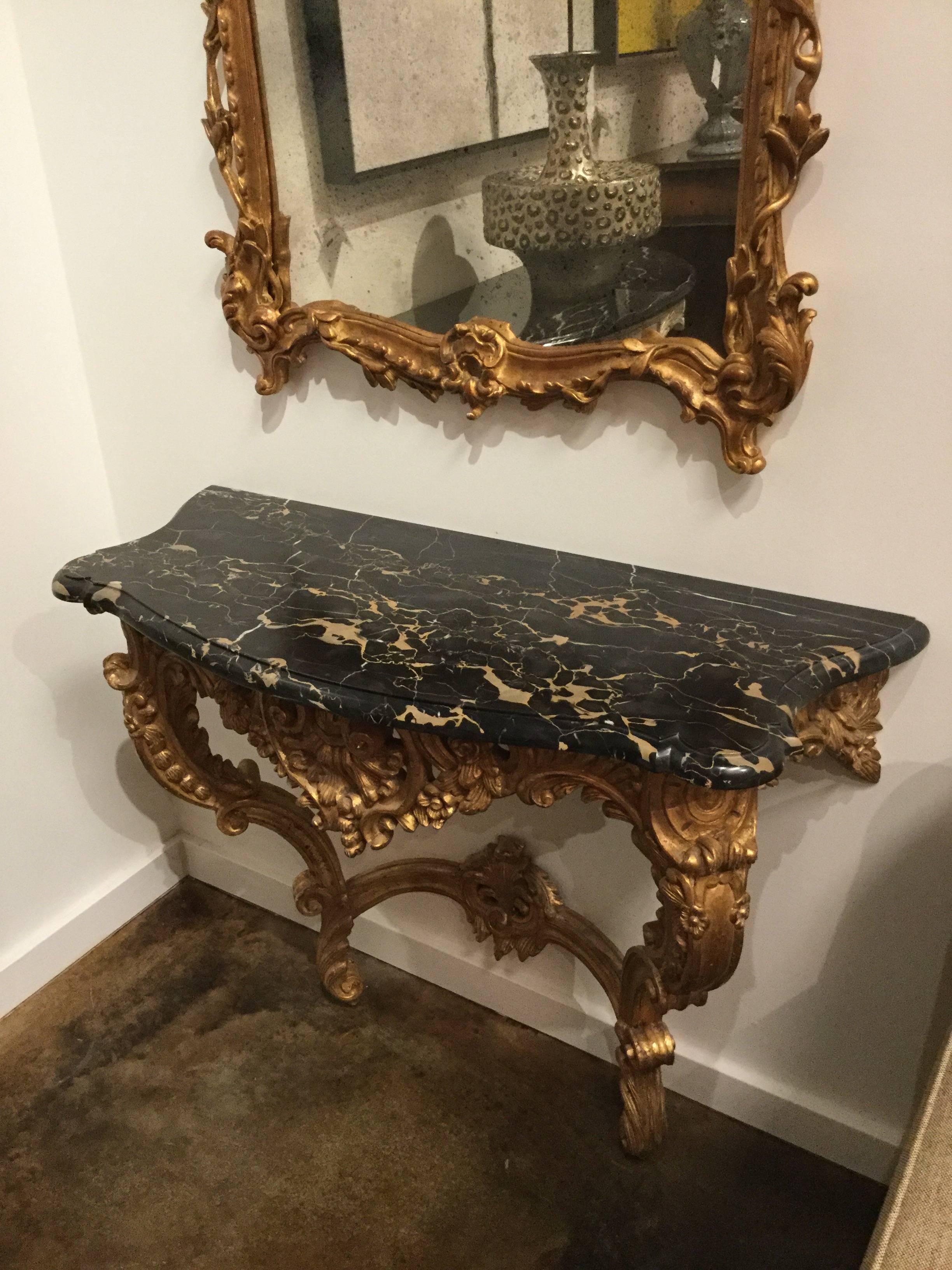 18th century style wall console heavily hand-carved with shells, rosettes and acanthus leaves, resting on two feet, finished in gold gilt and topped with a charcoal colored marble, Italy.