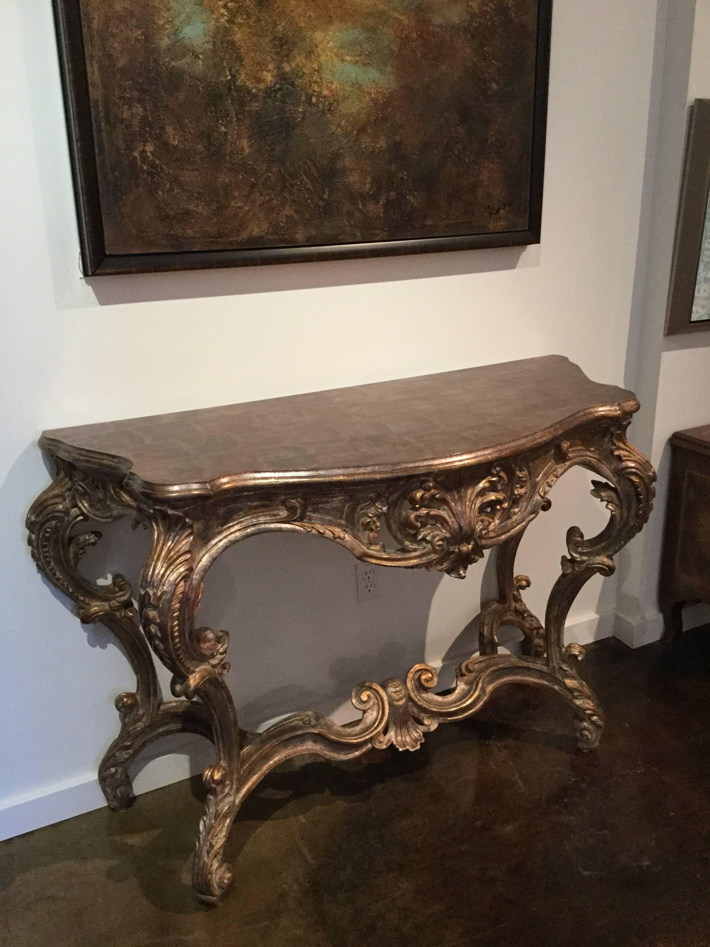 Rococo style wall console heavily hand-carved with shells, rosettes and acanthus leaves, resting on four feet, finished in as antiqued silver gilt and topped with a faux marbling texture, Italy, circa 1960.