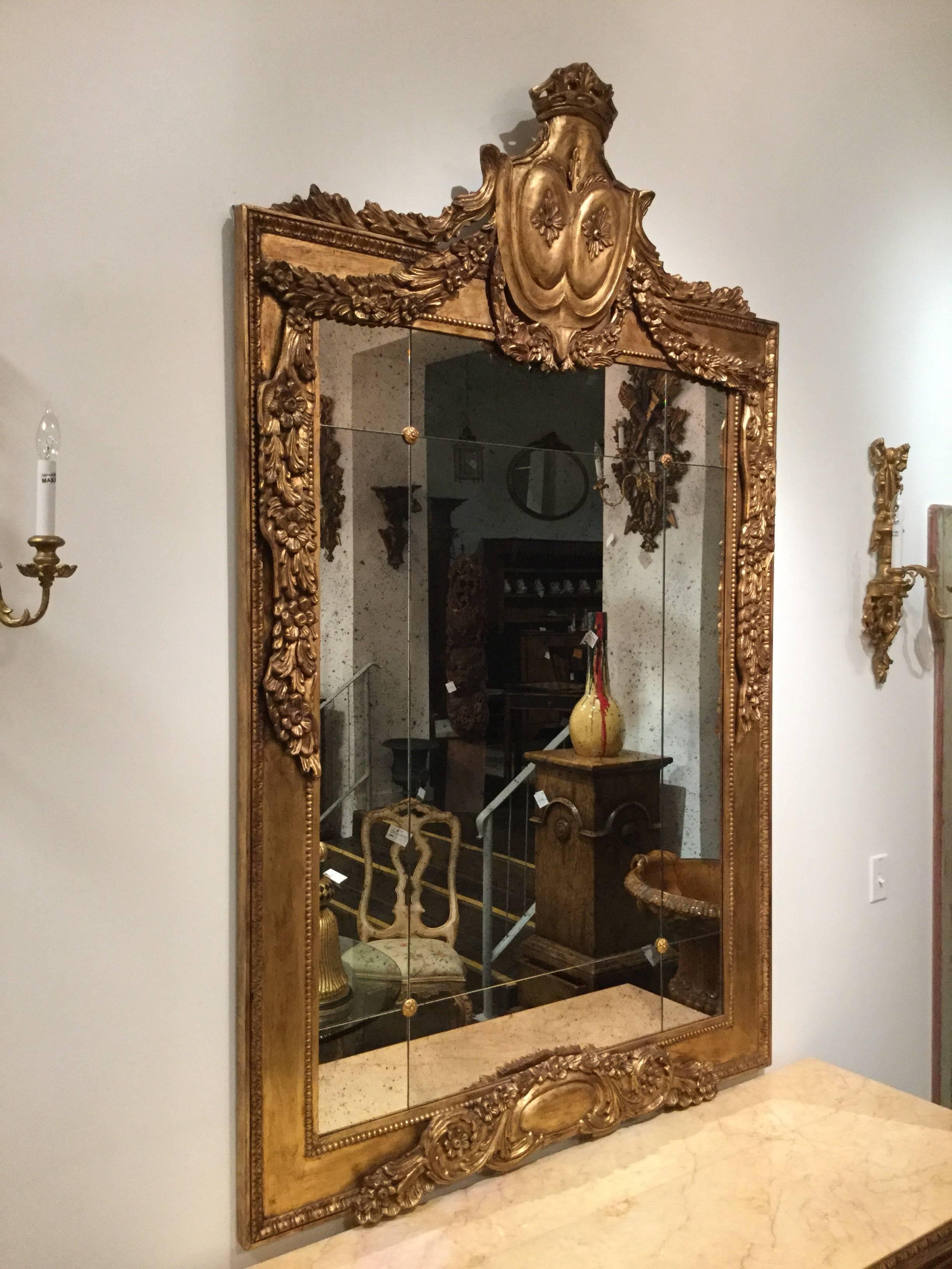 Magnificent Louis XVI style hand-carved mirror with rosettes and antiqued mirror inset, featuring an antiqued gold gilt finish, Italy.