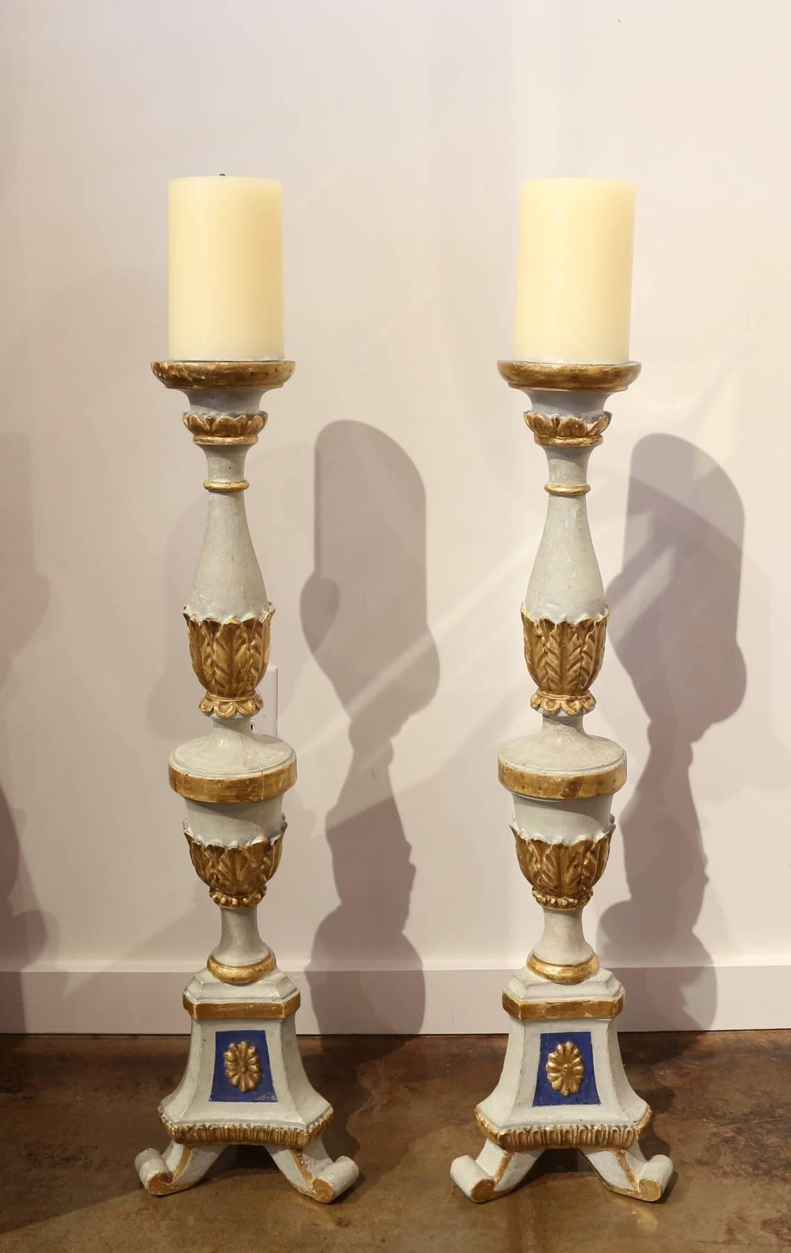 Pair of antique 19th century carved wooden altar candlesticks in an aged ivory color with gold leaf and lapis colored accents, Italy, circa 1870.