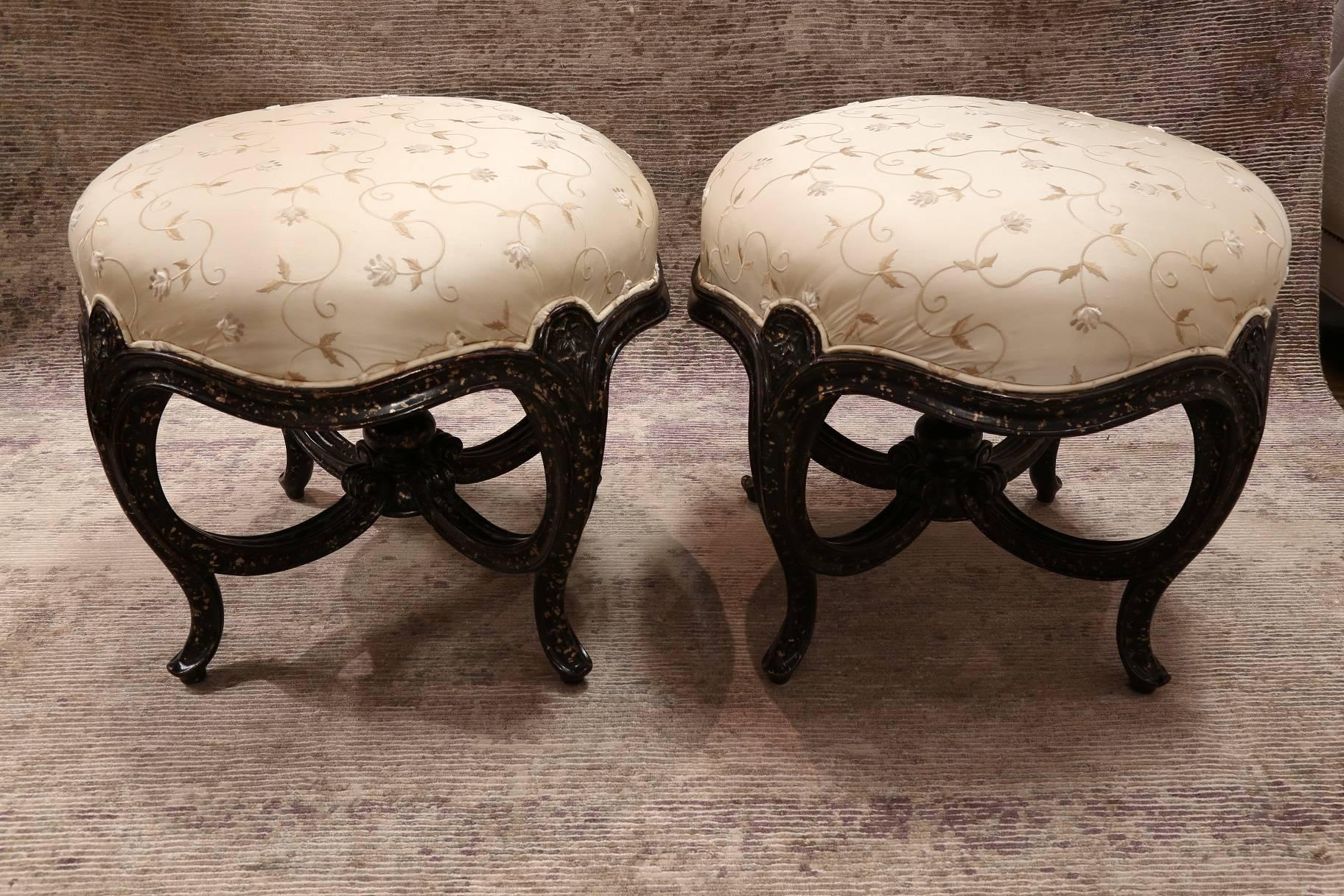 Pair of hand-carved round footstool with embroidered floral silk upholstery finished in a hand-painted distressed ebony featuring an elegant X-stretcher adorned with a finial, Italy.