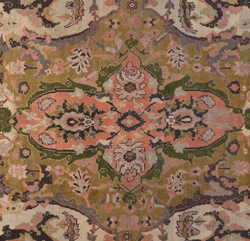 Handwoven antique Persian Sultanabad rug. The pink colored medallion is contained within a ivory field accented in shades of green, lavender, rust and blue. The border is ivory and rust with crown shaped motifs. Handwoven in Iran. circa 1900.
  