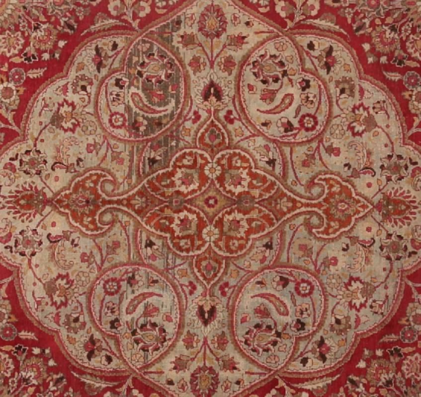 Handwoven old Persian Mashad rug featuring a scalloped medallion and pendants on a red colored field and beige border accented in shades of ivory, light blue, green, gold, burnt orange, teal and mustard, Iran, circa 1940.

