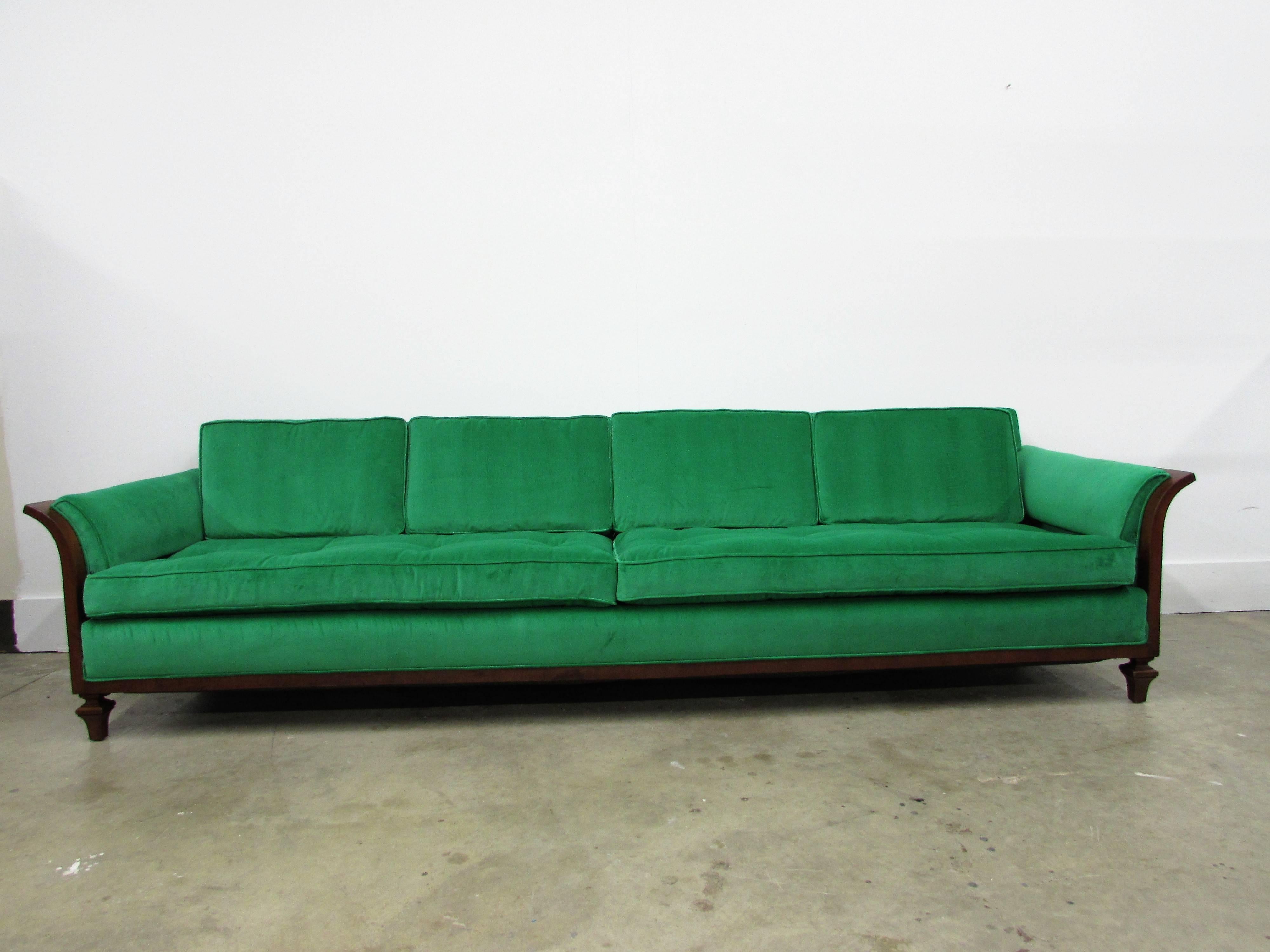 Walnut wrapped sofa by Tomlinson is this sophisticated and stylish Mid-Century Modern design, it has flared walnut sides, edges and ending in carved feet with newly reupholstered Kelly green velvet fabric with four top cushions and cording on all