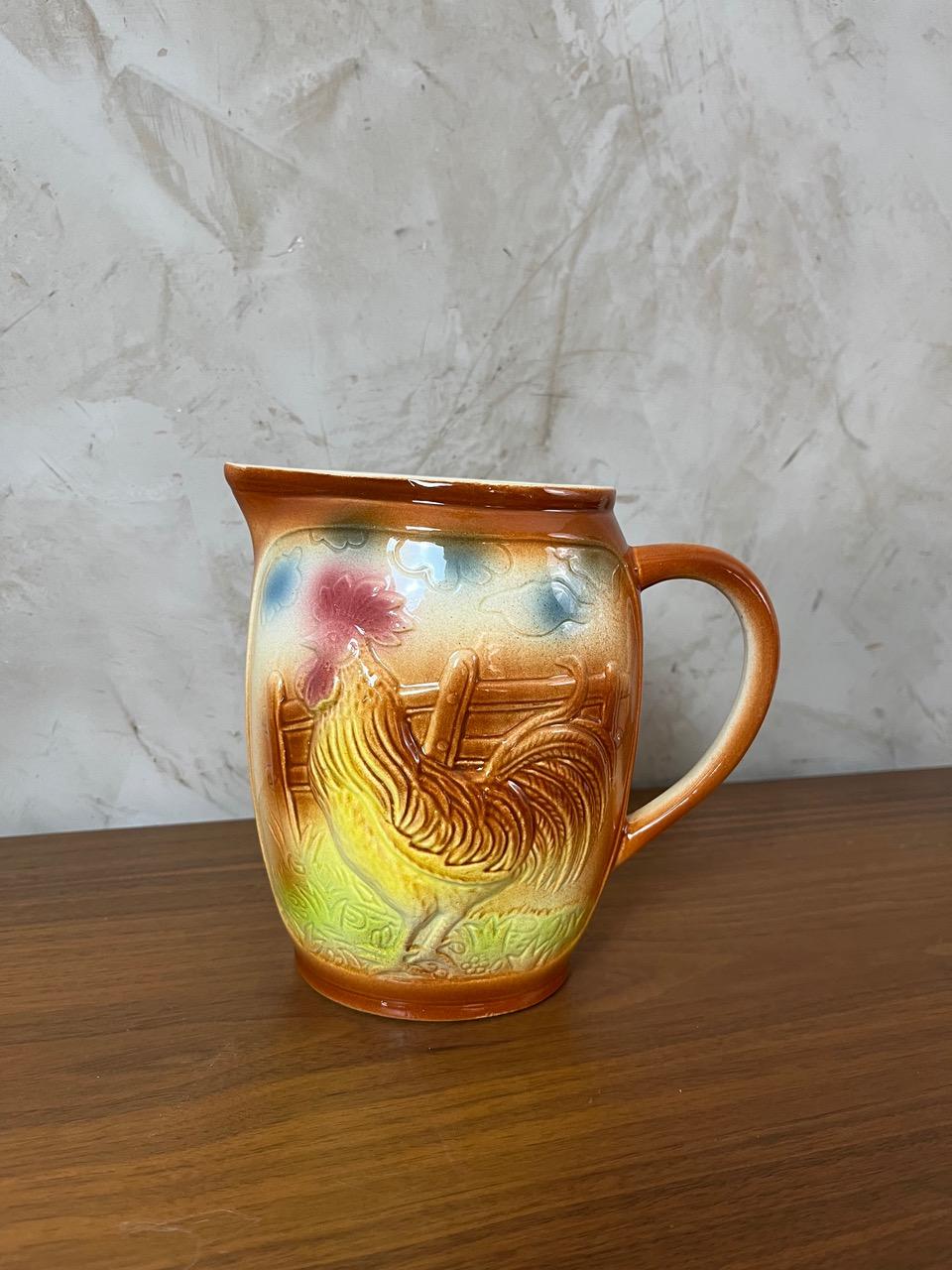 Pot à eau en majolique de Saint Clément au charme rustique et intemporel. Idéal pour la décoration d'une cuisine, d'un intérieur de style champêtre ou comme pièce fonctionnelle pour servir de l'eau, de la limonade ou du vin. Le motif est un coq.