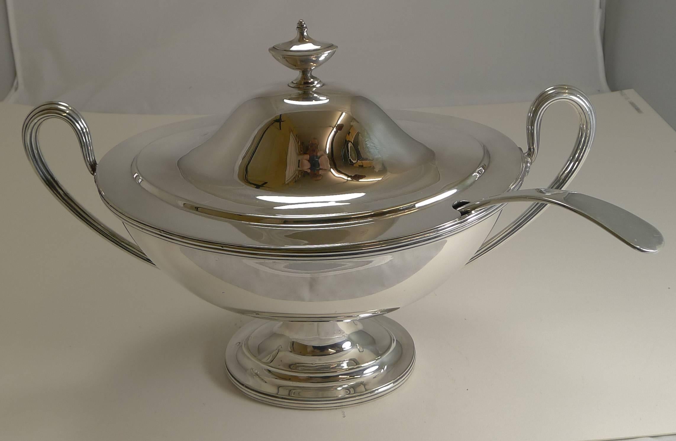 An Edwardian silver plated Neoclassical style soup tureen, having a pull-off lid with an urn-shaped finial and cut-out slot for a ladle and two reeded scroll side-handles, and all sitting on a pedestal foot. The interior is washed in gold.

My