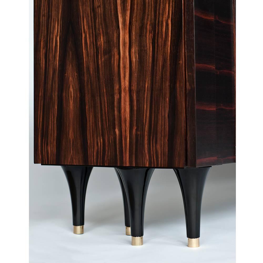 The Pegu cabinet or credenza by DeMuro Das has sculpted, multi-layered doors in hand-laid matte Macassar ebony. Turned legs in glossy black lacquer with bronze caps support this piece. This case piece features four push-open doors and two adjustable