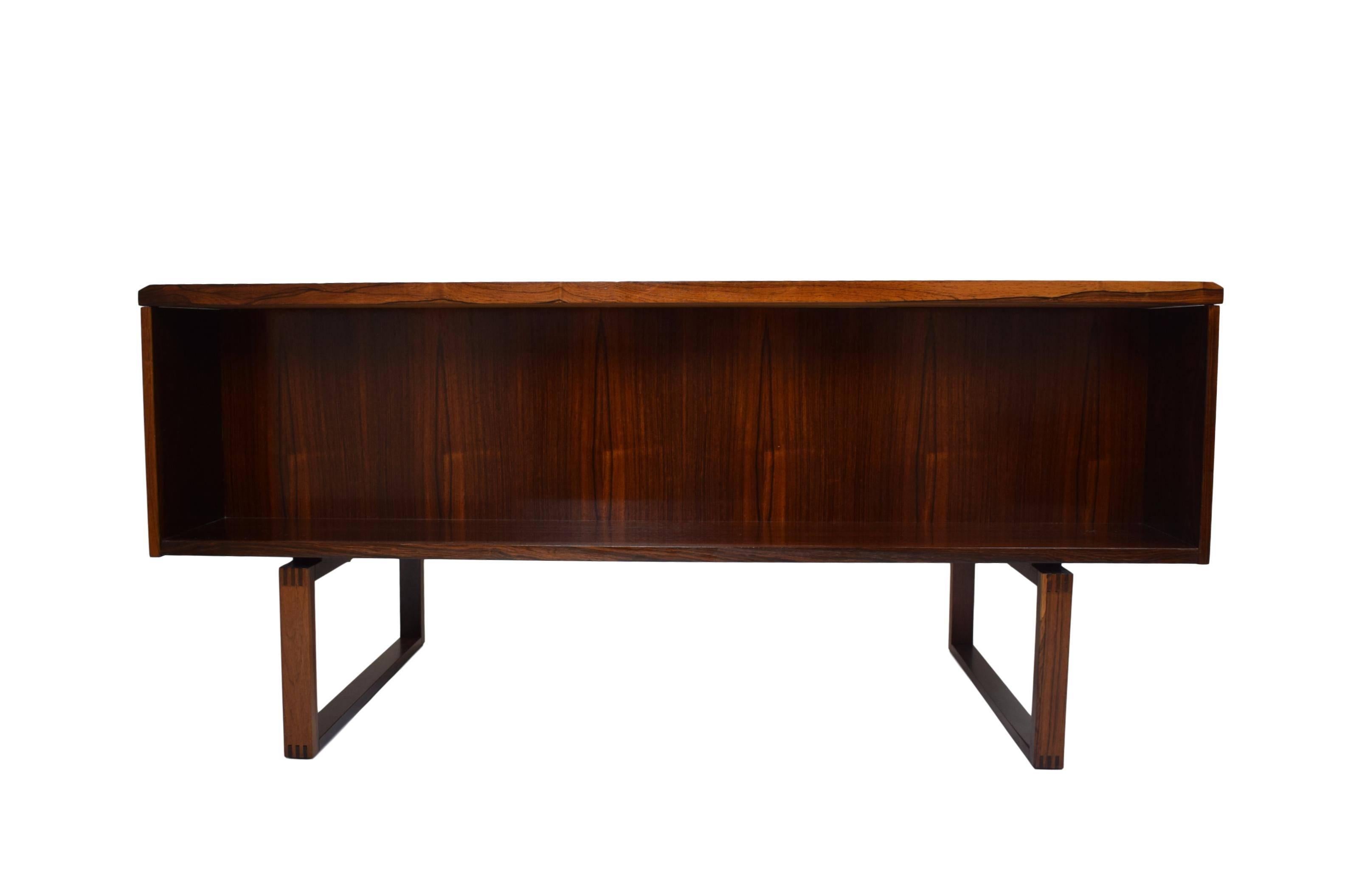 A Danish midcentury rosewood desk by Henning Jensen (1924) and Torben Valeur (1920-2000). Six drawers on the front and one large storage compartment on the rear. Rosewood veneer and solid rosewood legs/ drawer handles. Legs and handles with finger