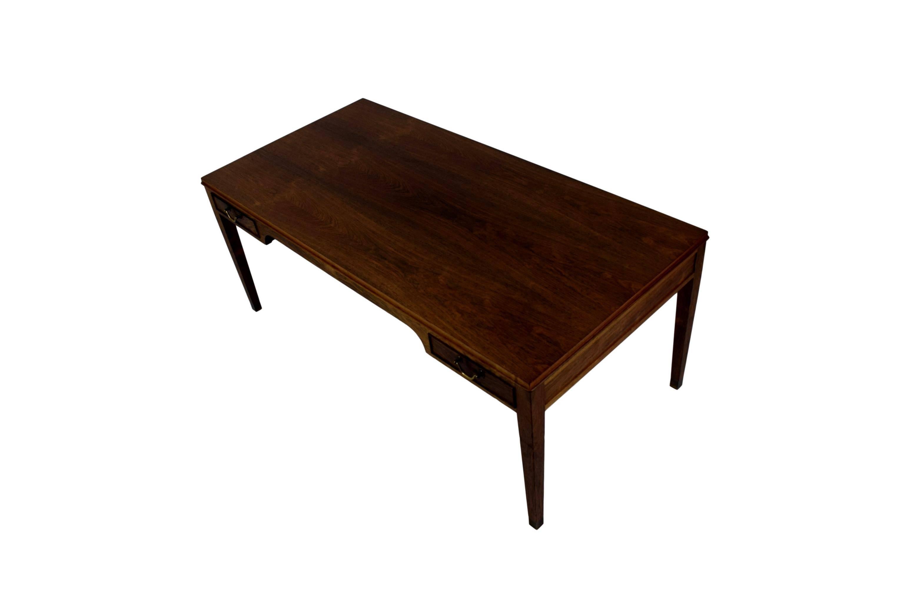A Danish midcentury rosewood coffee table by Frits Henningsen. Rosewood veneer and solid rosewood legs. Four drawers with brass handles. Tapered legs with brass shoes.

