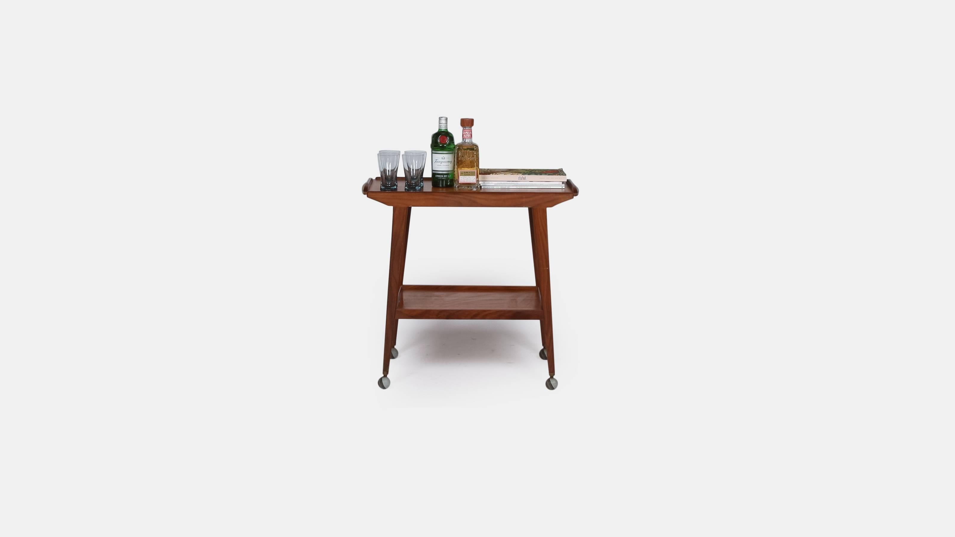 A midcentury teak drinks trolley of angular form on tapering legs and having twin tiers.

Great as a mini cocktail bar in your sitting room.

Nice clean lines mean this drinks cart would work well in midcentury and contemporary interiors.